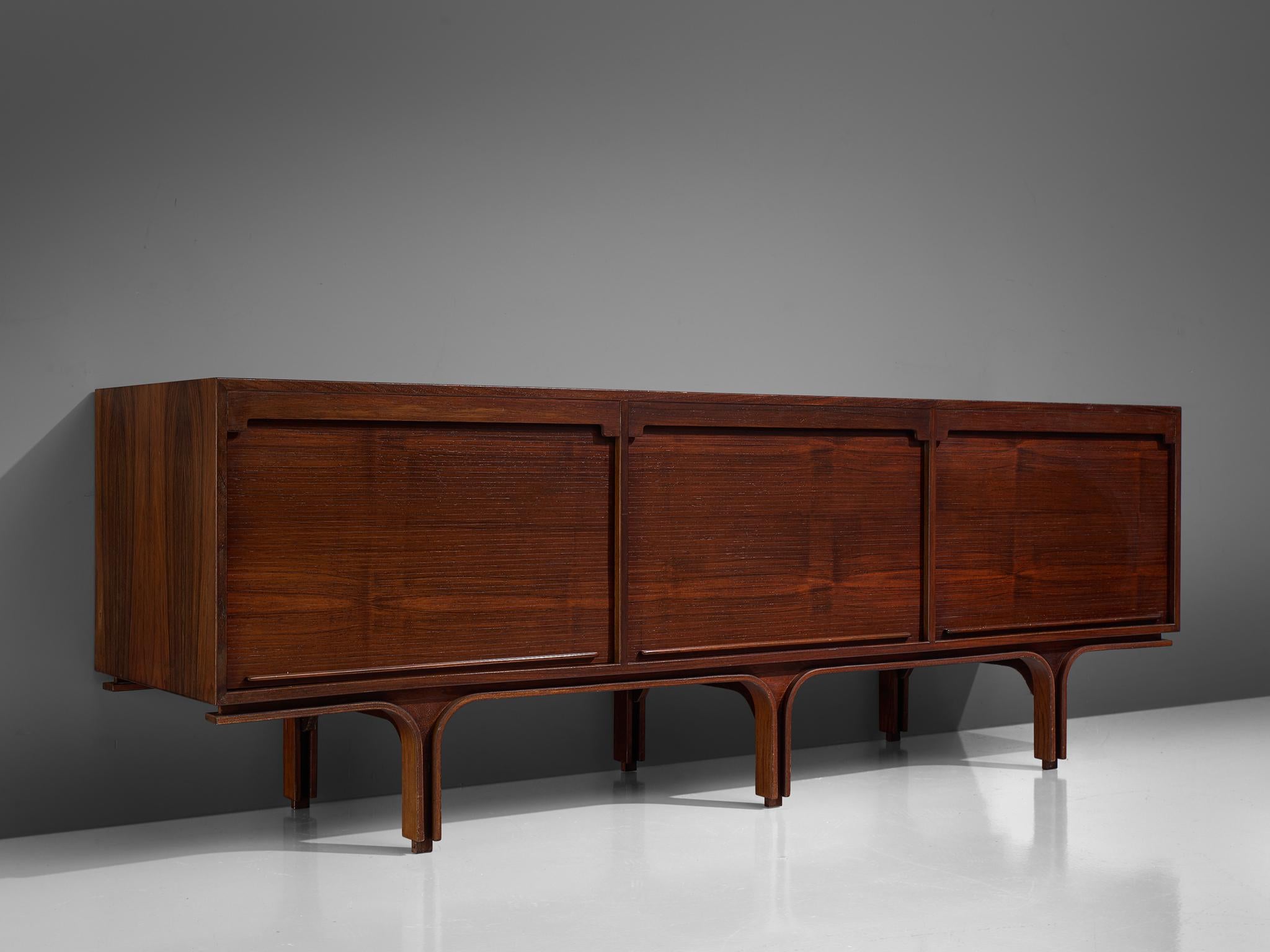 Gianfranco Frattini for Bernini, credenza, rosewood, Italy, 1960s.

This credenza in rosewood is designed by Frattini. It features the typical design traits of Frattini such as the tambour doors but also the legs that feature a border with