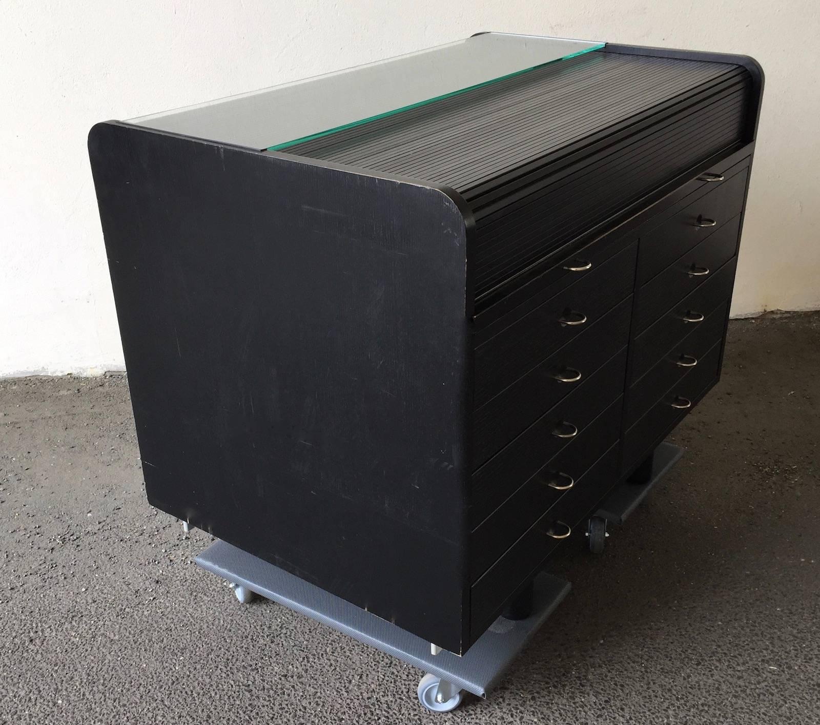 Ebonized wood, leather an aluminum. The secretary is a practical piece of furniture as it offers plenty of storage space. On the front side there are ten large drawers. A writing surface can be pulled out that opens the secretary. A writing section
