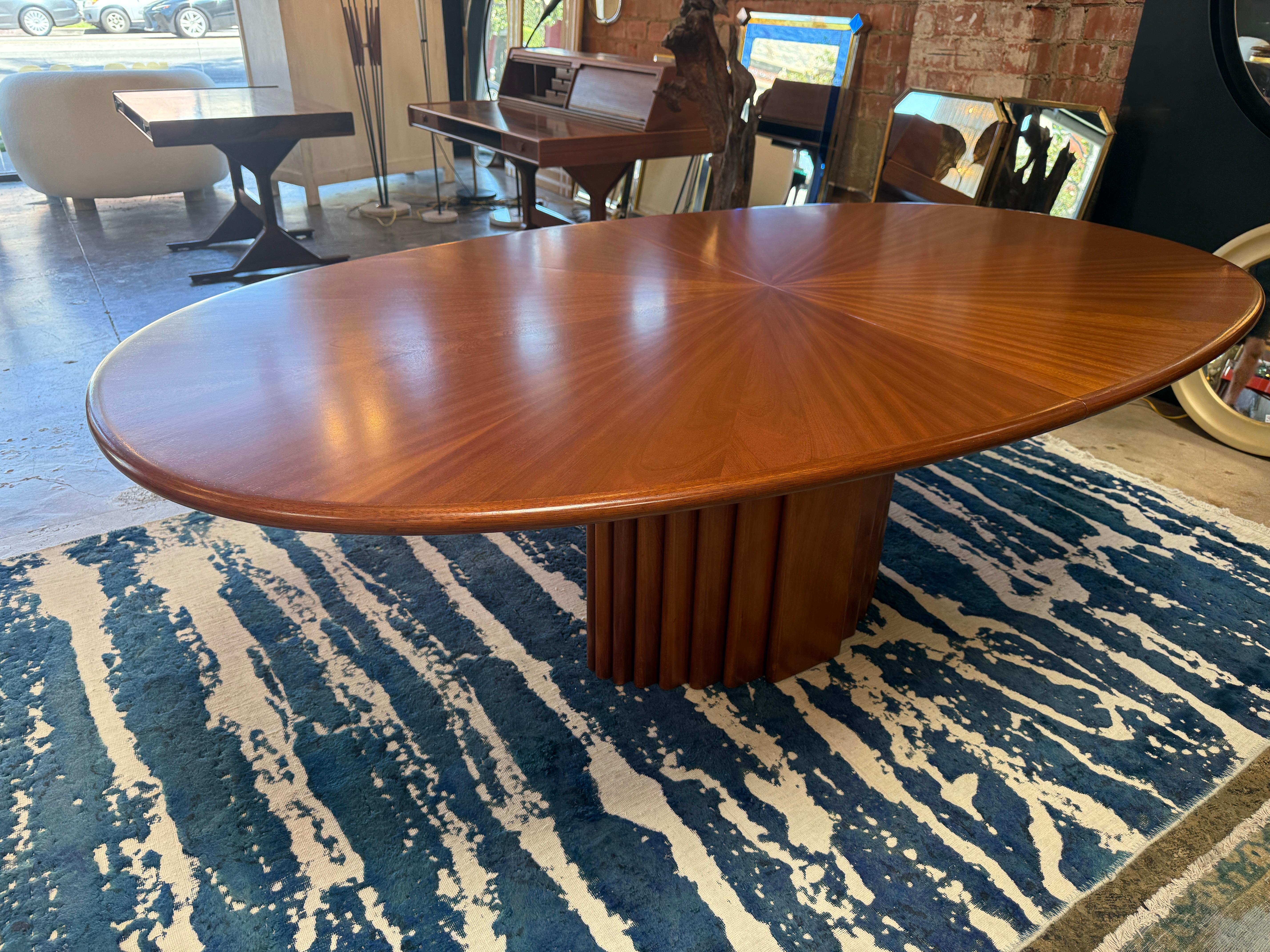 A refined Italian dining table by Gianfranco Frattini, crafted in walnut during the 1970s. The oval tabletop is distinguished by a dramatic sunburst veneer pattern that radiates from the center, enhancing the natural grain with remarkable depth and
