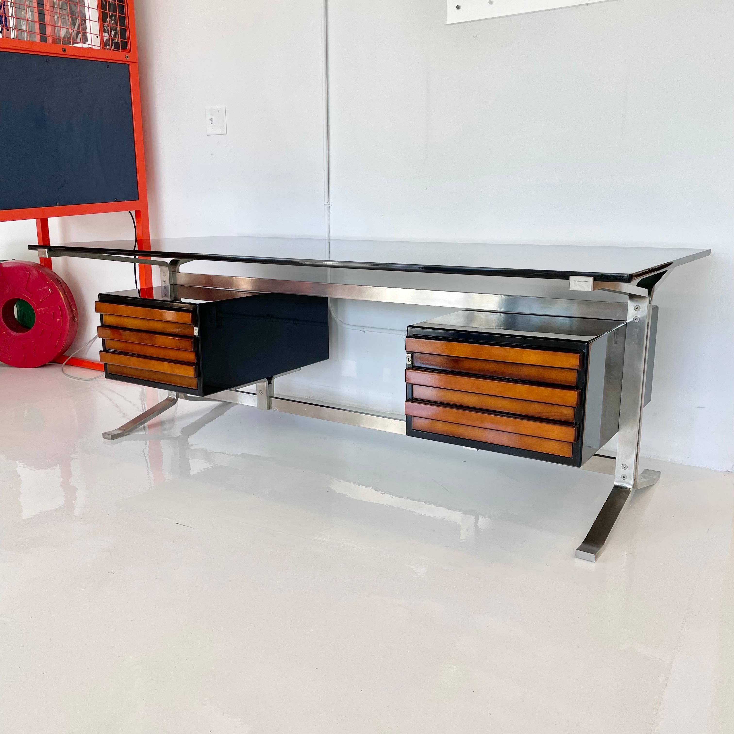 Stunning Formanova desk by Gianni Moscatelli. Prominent 3/4 inch smoked glass desk top floats on top of newly polished stainless steel base. Three pull-out drawers on either side are in the original caramel wood and are encased by a beautiful ebony