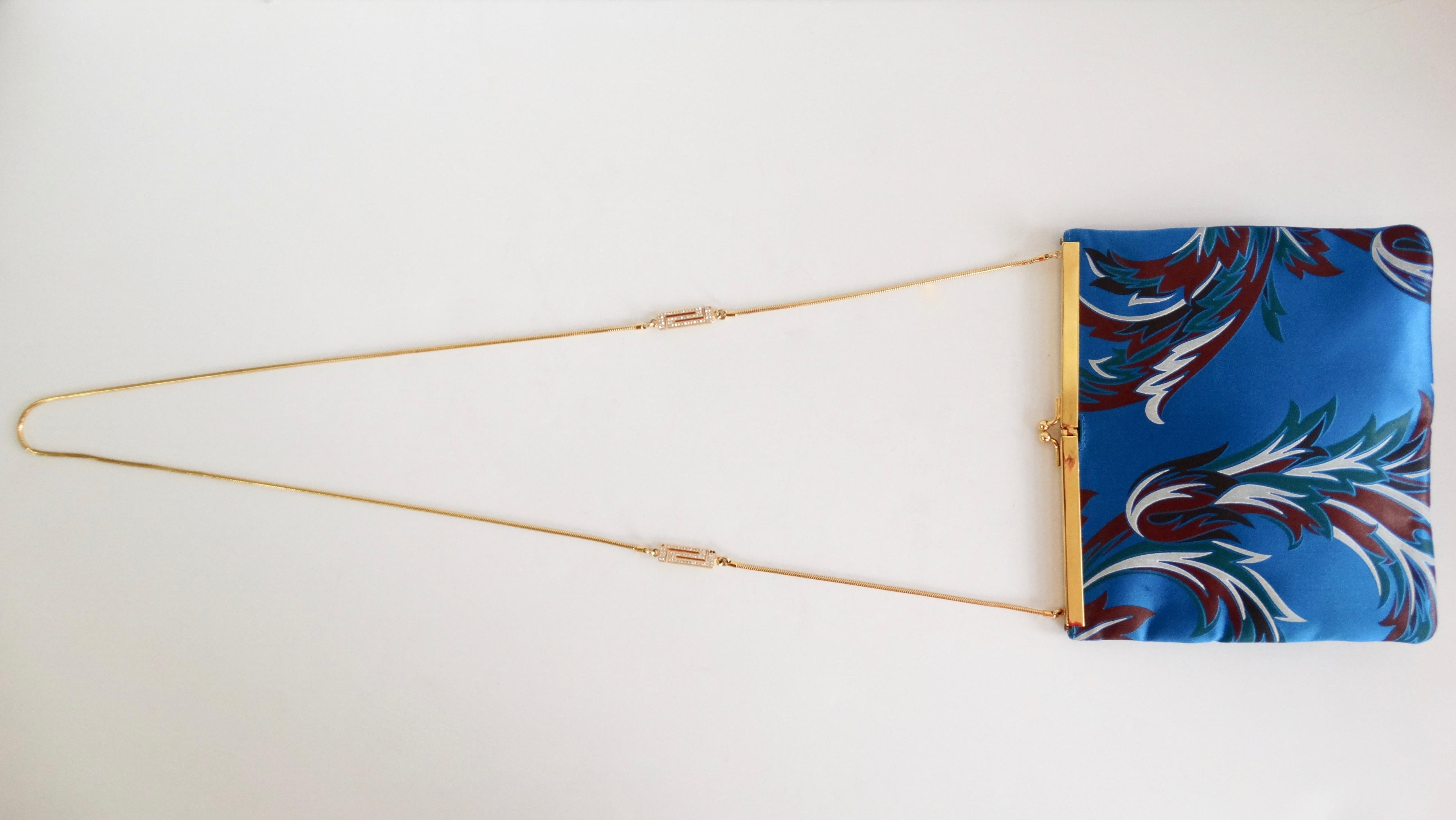 Élevez votre look avec ce magnifique sac à bandoulière Versace ! Circa 1990, ce sac est fait d'un magnifique satin bleu et présente un motif baroque multicolore. Il est doté de ferrures dorées, d'un fermoir à baiser et d'une lanière en chaîne ornée