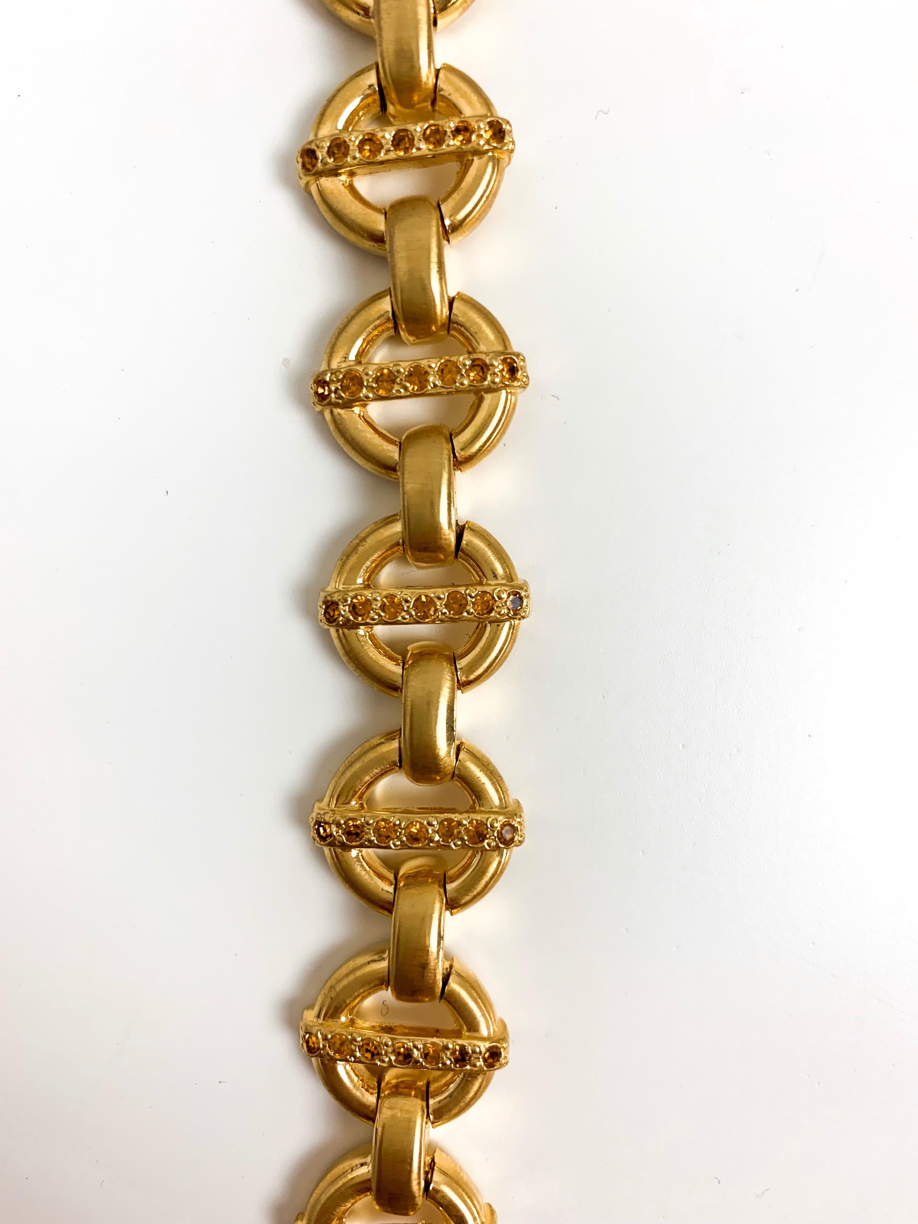 Diese seltene Gianni Versace Halskette ist ganz im Stil des Designers selbst. Die goldene Halskette aus den 1990er Jahren zeichnet sich durch eine schöne, kreisförmige, ineinandergreifende Kette mit orangefarbenen Kristallen aus. Dieses schlichte