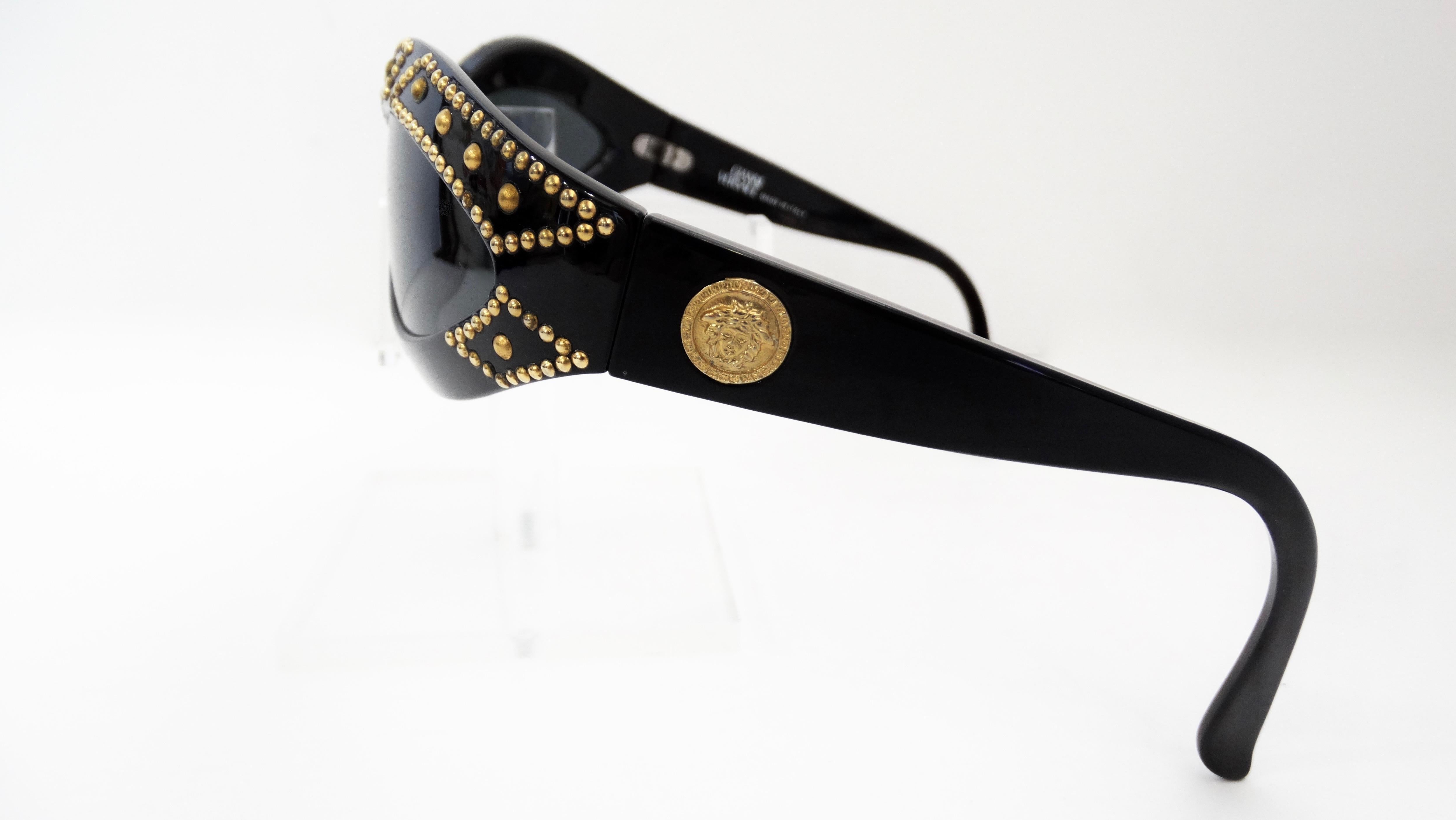 Spice up your sunglasses game with a piece from the Versace archives! Circa 1990s, these wrap style sunglasses feature an acrylic black frame with black lenses. Frames are embellished with gold studs with a Medusa embossed coin on both arms. The