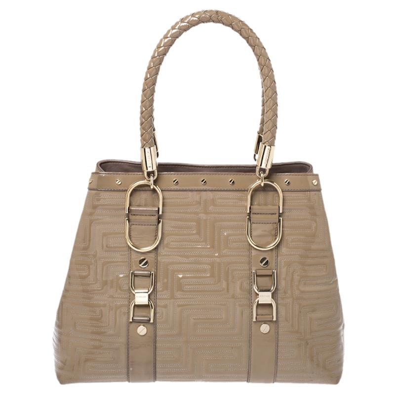 How gorgeous is this satchel from Versace! It carries an outstanding design and a fabulous interplay of patent leather and gold-tone hardware. It has a top leading to a satin interior while being held by two top handles. The shape and the brand logo