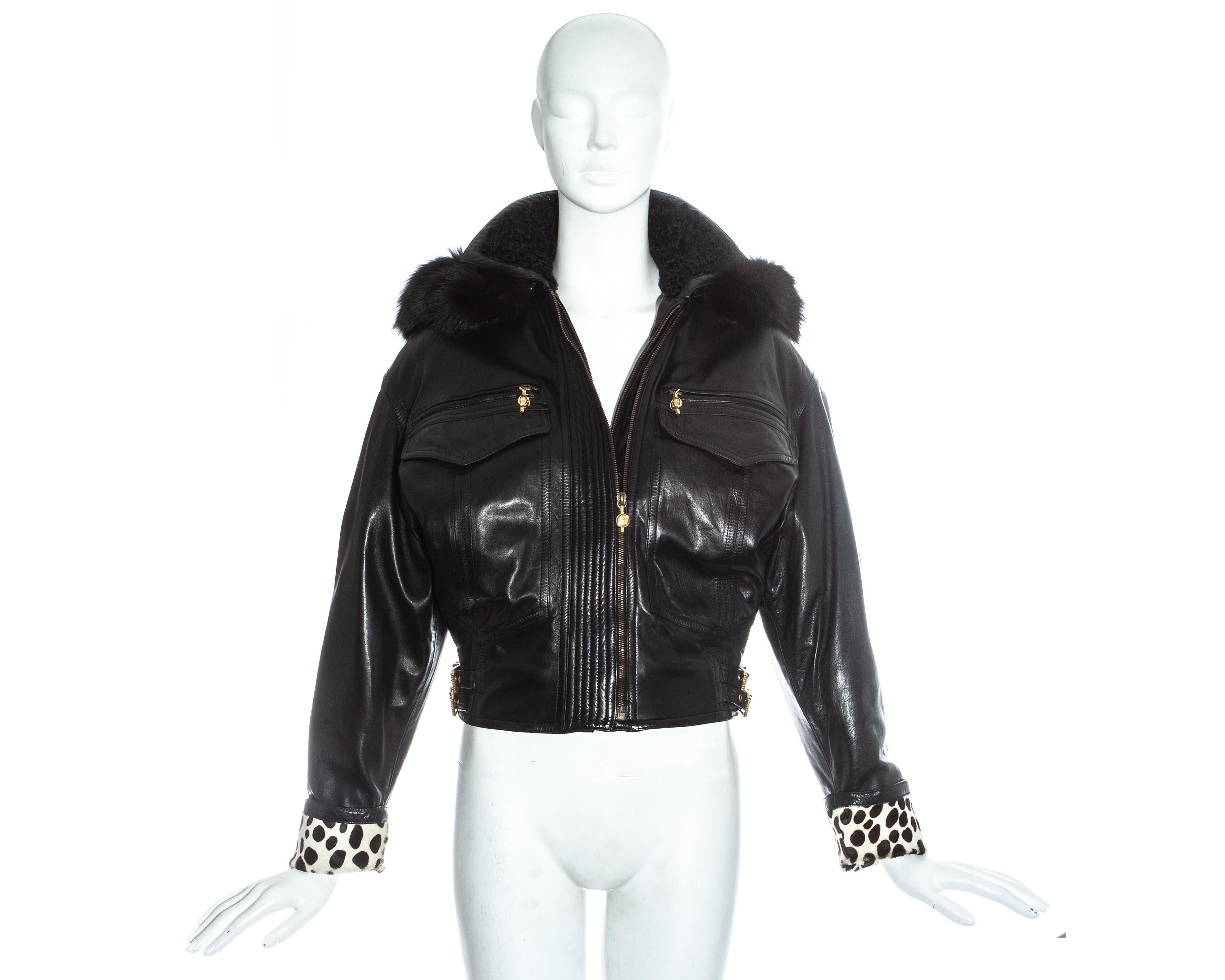 Gianni Versace black leather bomber jacket with signature Versace western-style gilt buckles to waist, two front pockets with gilt Medusa head zip pulls, spotted ponyhide cuffs and detachable fur-lined hood.

Fall-Winter 1992 