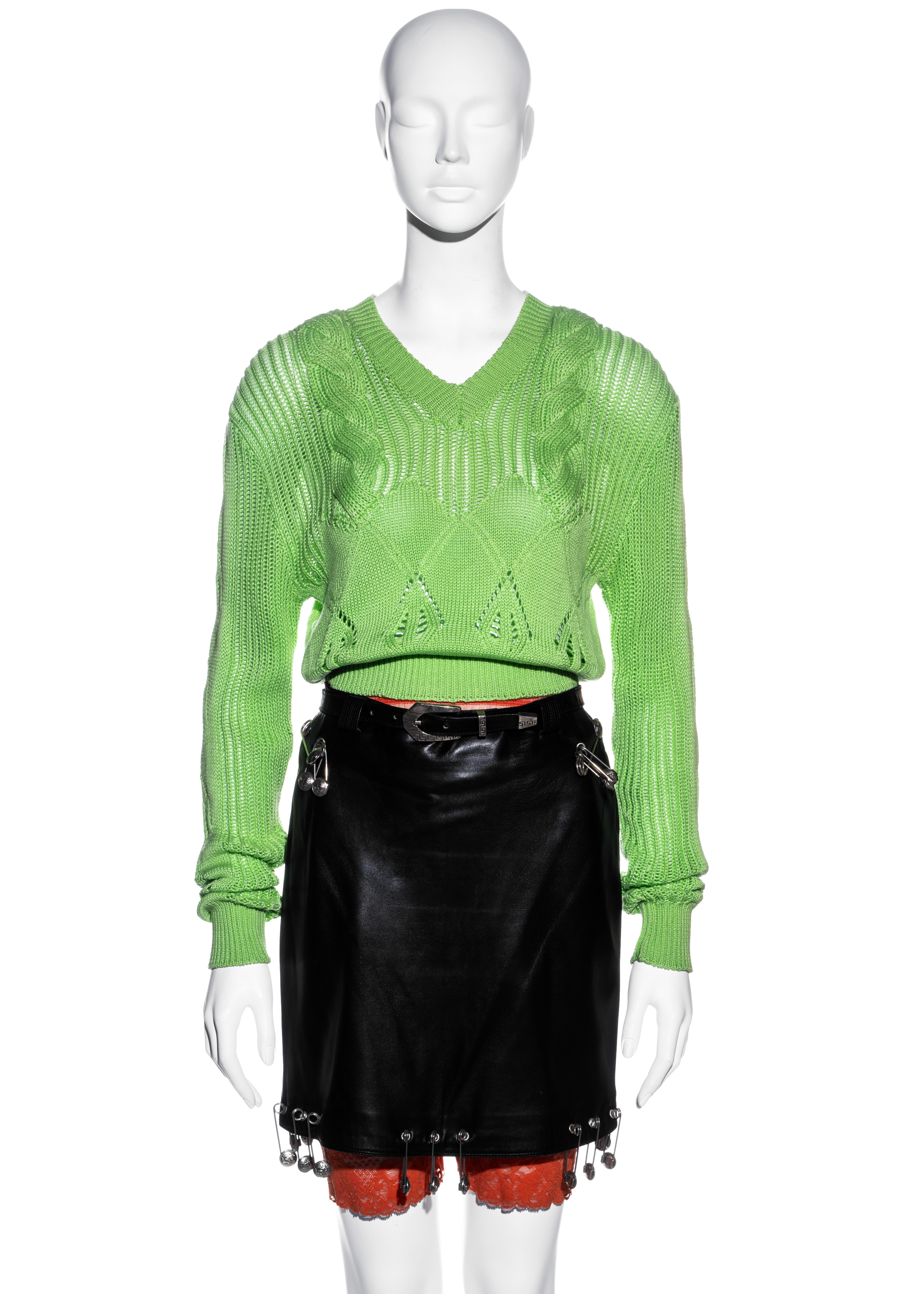 ▪ Gianni Versace runway ensemble 
▪ Black leather pencil skirt 
▪ Neon green knitted v-neck sweater 
▪ Orange mesh cycling shorts with lace trim 
▪ Large silver Medusa safety pin adornments 
▪ IT 42 - FR 38 - UK 10 - US 6
▪ Spring-Summer 1994