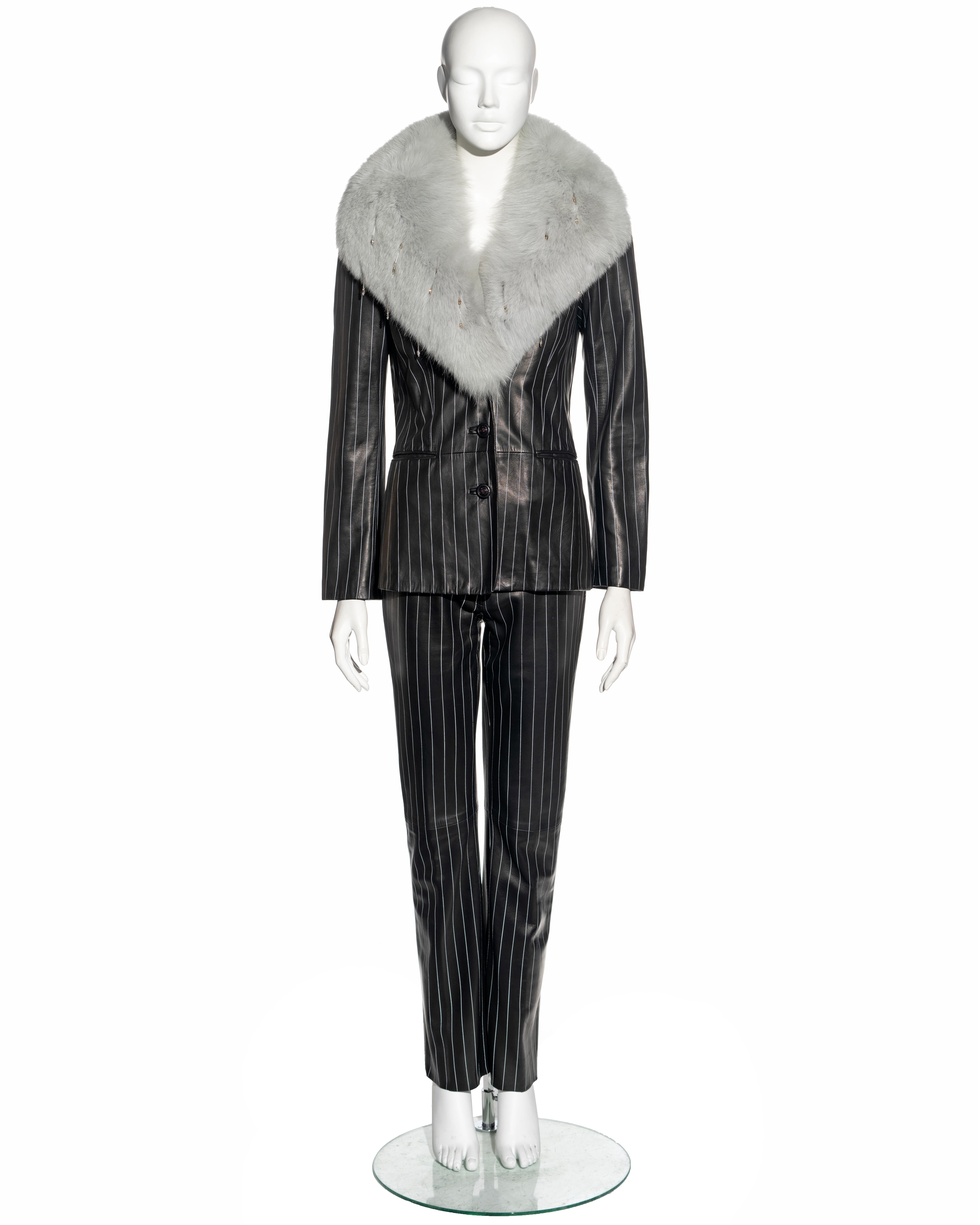 Abito di Gianni Versace
▪ Disegnato da Donatella Versace
Realizzata in pelle di agnello nera con gessature dipinte. 
Grande colletto in pelliccia di volpe impreziosito da nappe con perline trasparenti
Giacca blazer monopetto 
Pantaloni a gamba tesa