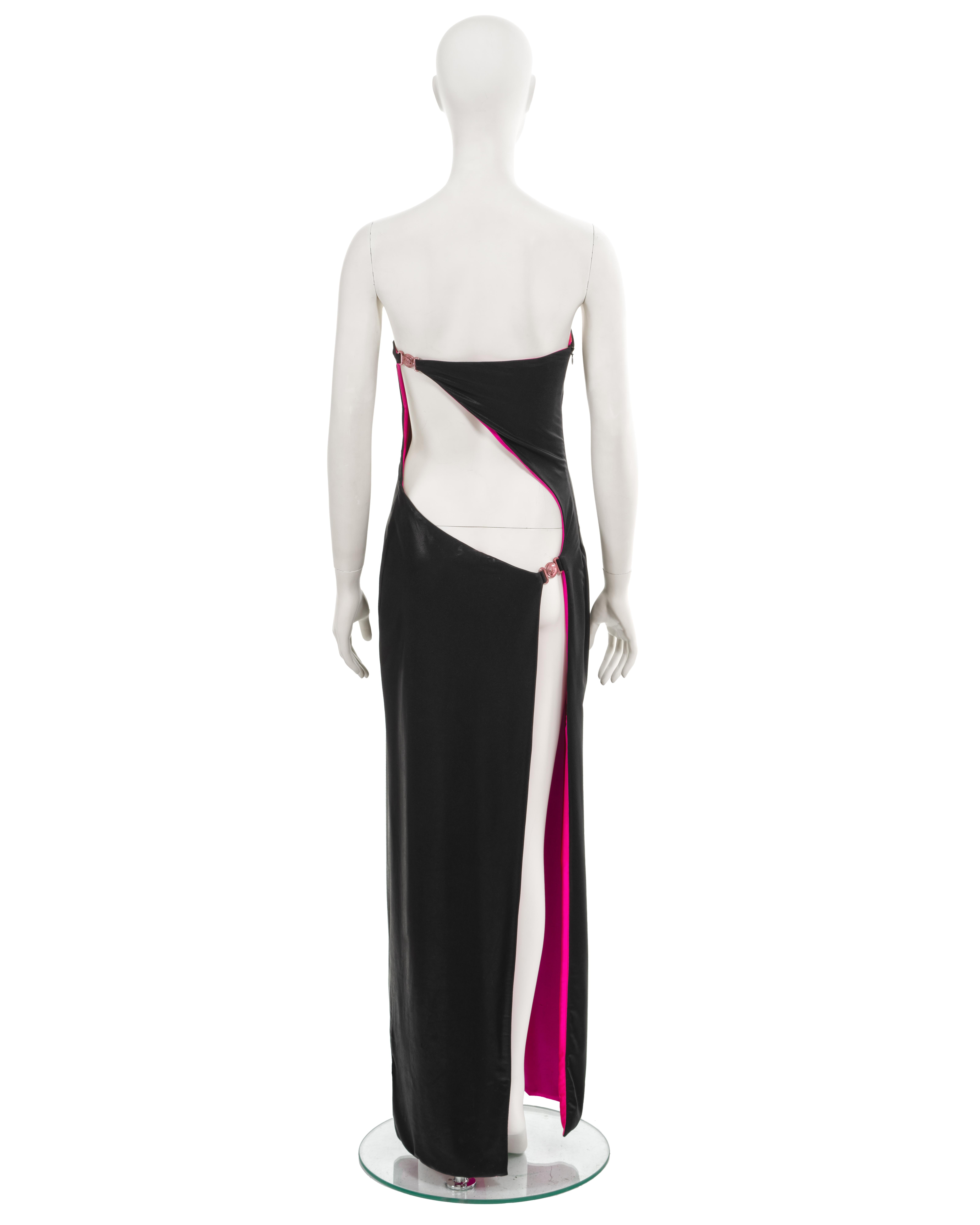 Robe du soir à bretelles d'archives de Gianni Versace, confectionnée en jersey stretch noir d'aspect mouillé et complétée par une doublure rose vif. Cette robe exquise présente une élégante découpe dans le dos, ornée de méduses en or rose, ainsi