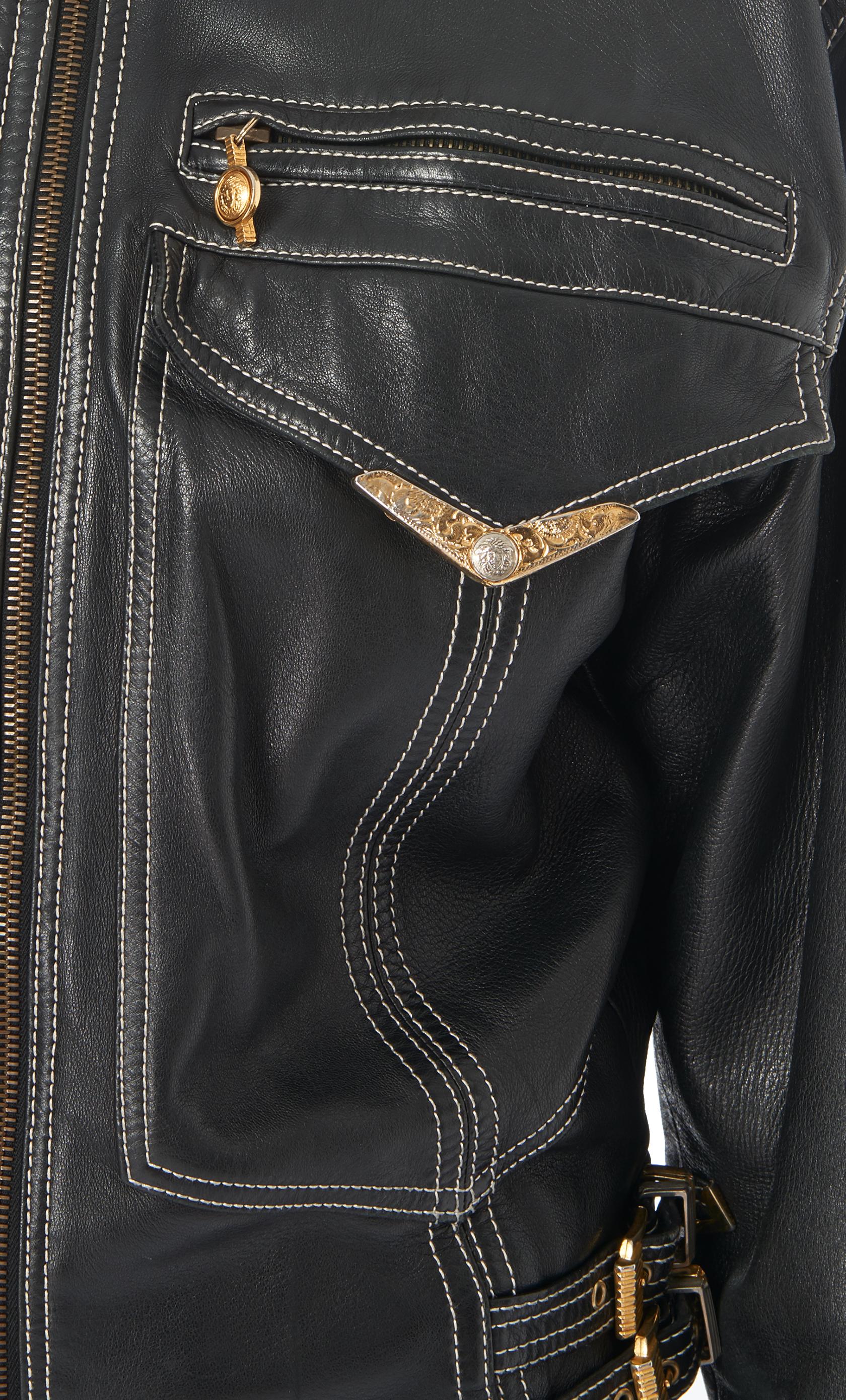 A Gianni Versace black leather Bondage jacket from Gianni Versace's Autumn/Winter 1992 Bondage collection. Featuring a pointed collar, long sleeves, a front zip fastening, front flap pockets, white detail stitching and gold and silver tone Bondage