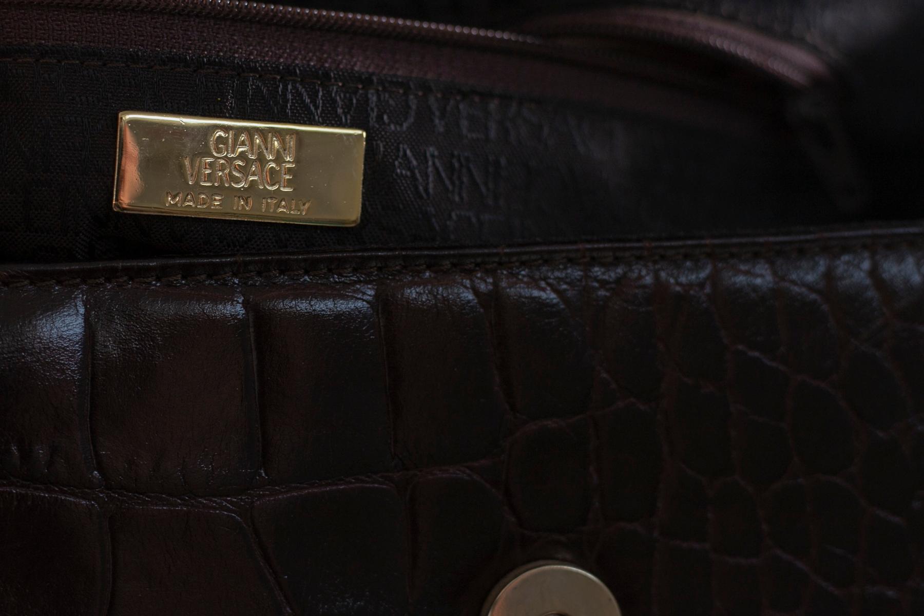 Étonnant et rare sac à poignée conçu par Gianni Versace dans les années 1990 en faux cuir imprimé crocodile bordeaux.
Le sac est de taille moyenne à petite et a la forme d'un sac bowling avec une double poignée entrelacée de chaînes dorées très