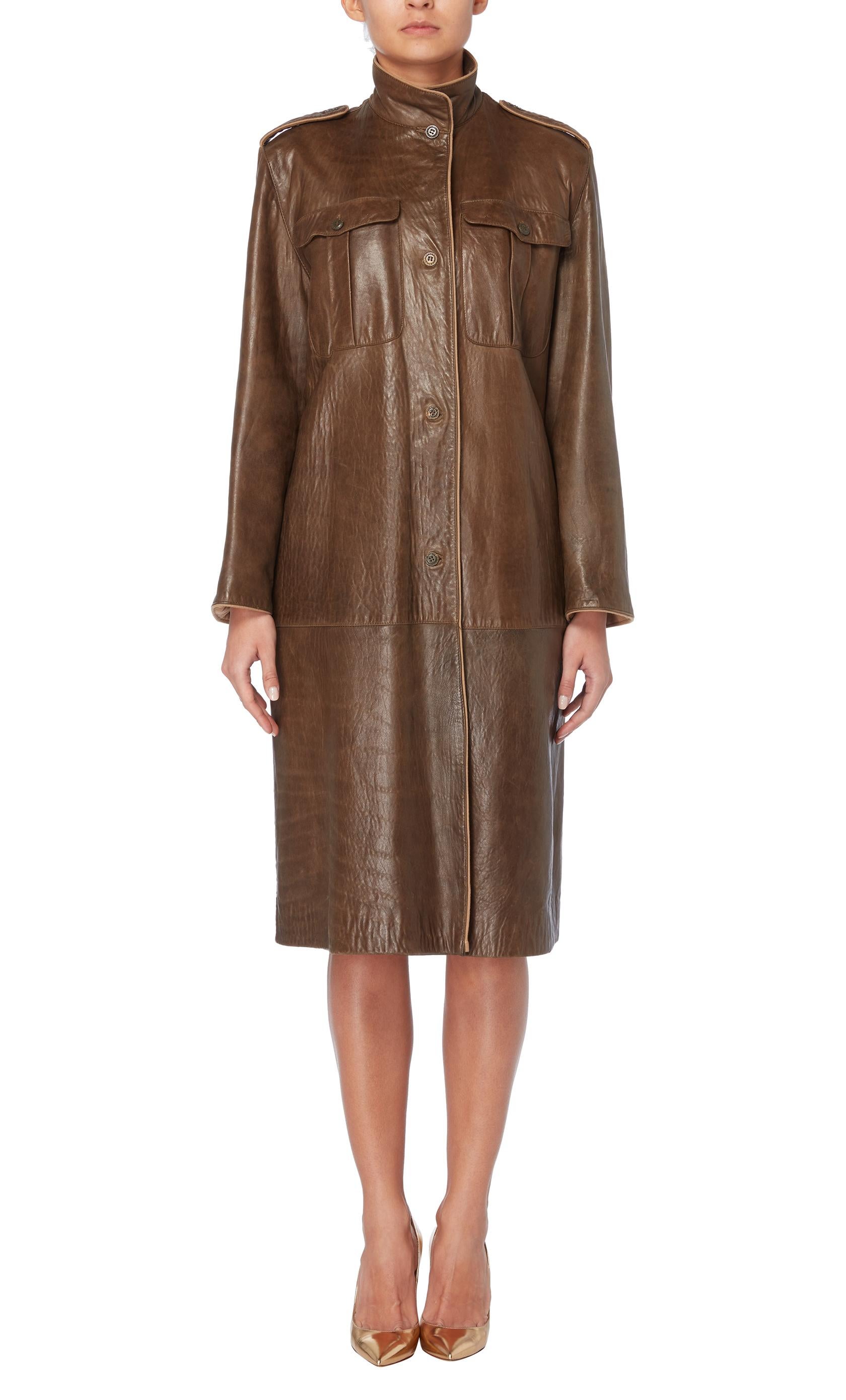 An early example of Gianni Versace's work, this brown leather coat if from the Autumn/Winter 1982 collection. Featuring a funnel neck, epaulettes and chest pockets, the coat has a military style and fastens with buttons to the front.