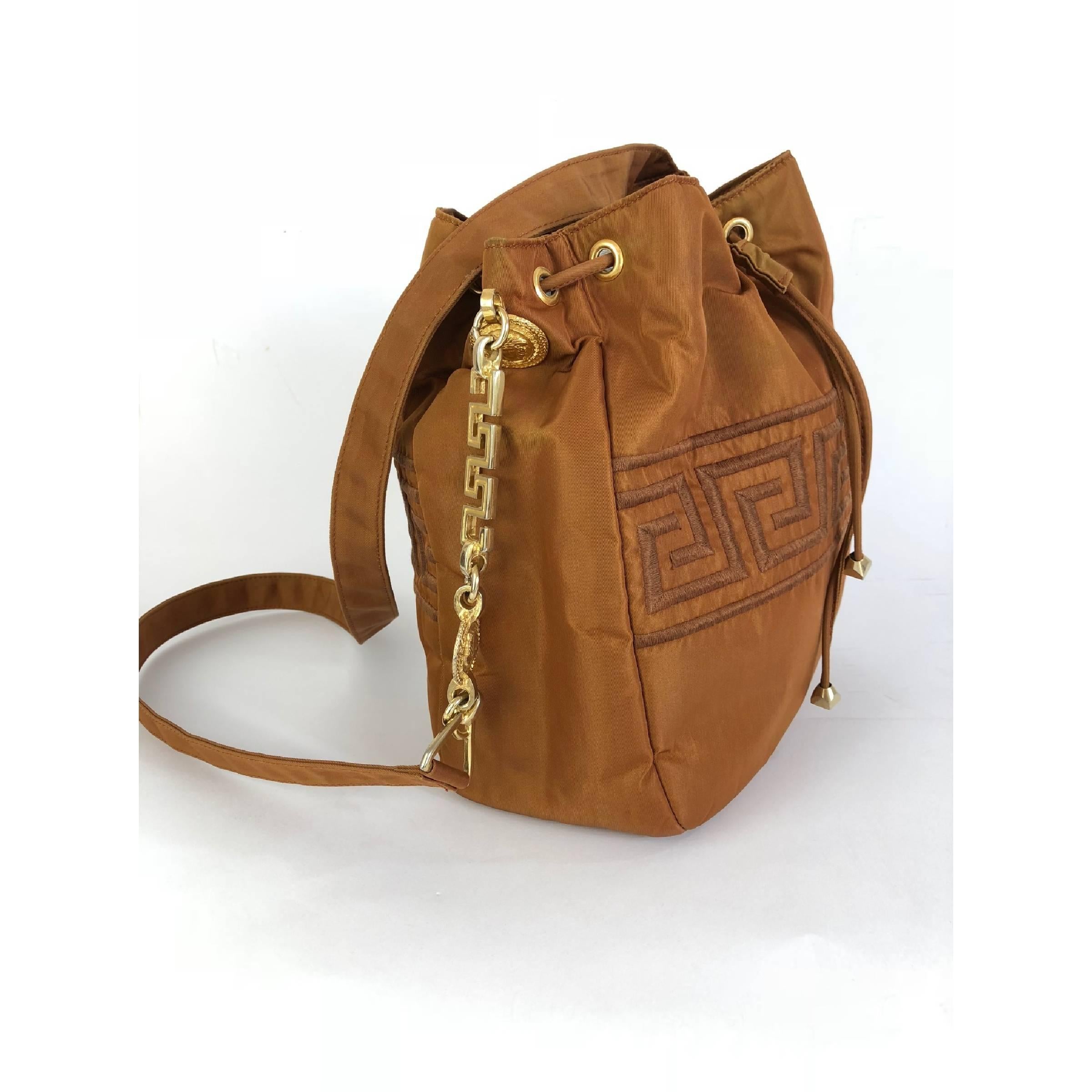 Gianni Versace bucket bag. Brown, satin-like material. Closure with drawstring, inside a small pocket and internal lining with logo. Gold-colored details with medallions depicting the jellyfish along the shoulder strap. There are some small stains