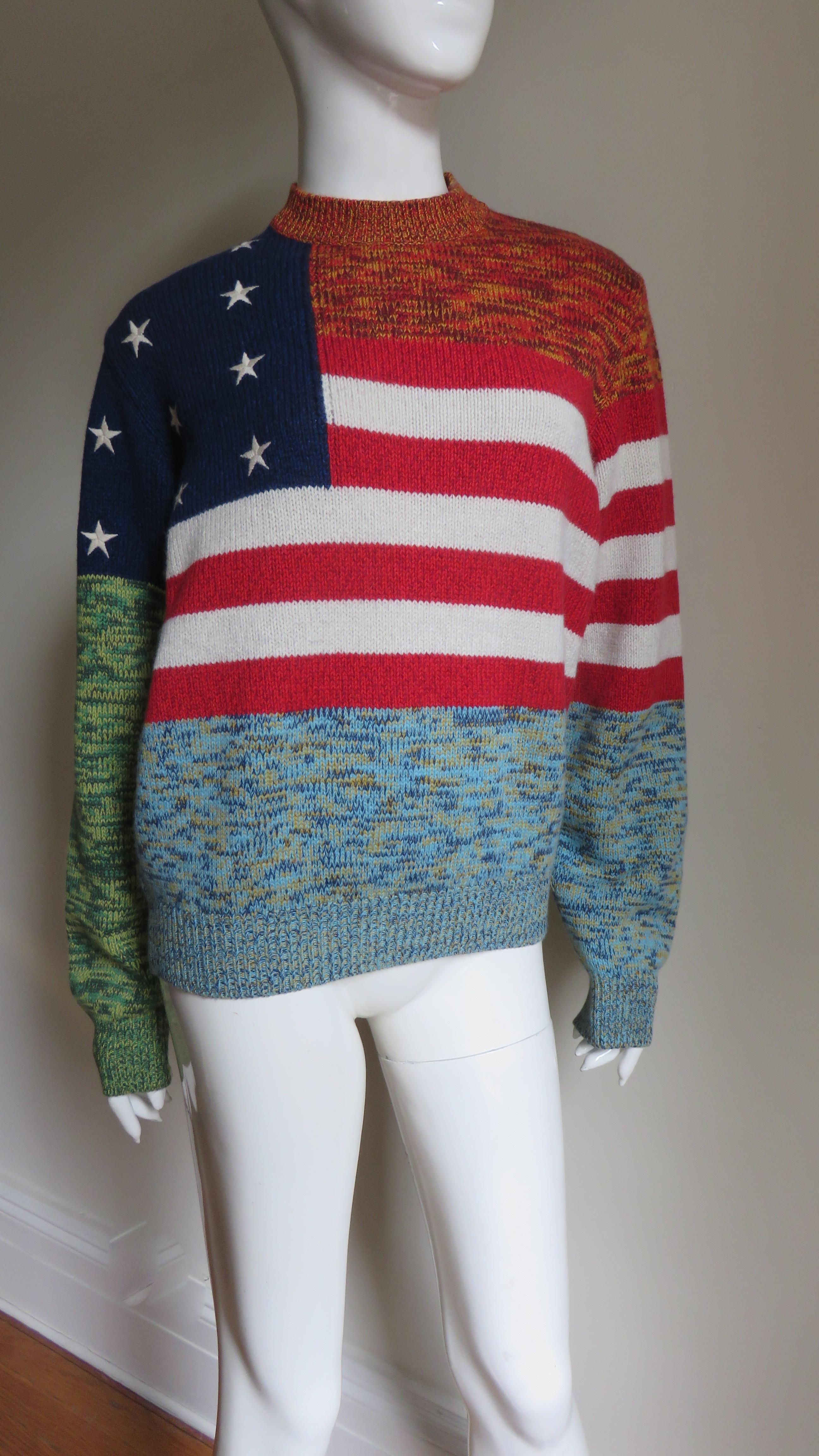 A fabulous cashmere American flag sweater from Gianni Versace. It has a flag on the front and back with red and white stripes crossing the chest, back and one sleeve and the white stars embroidered navy portion falling on one shoulder and upper arm.