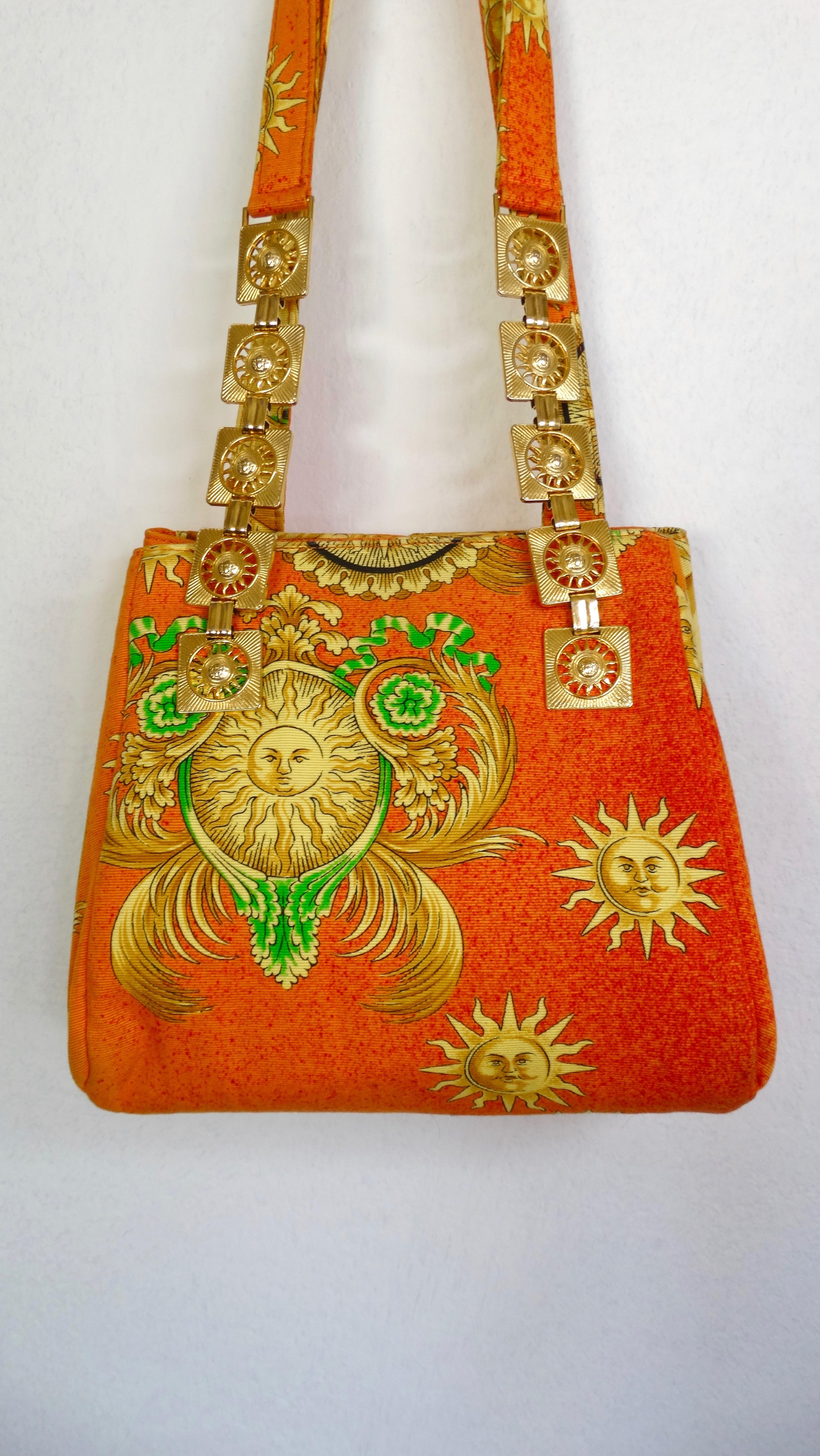 The ultimate summer handbag! Circa 1990s, this rare Versace handbag is a bright orange color and features a celestial sun pattern with green and gold Baroque designs. Includes two shoulder straps, a snap button closure and the front strap features