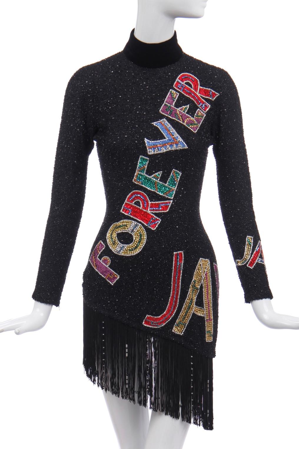 Atelier labelled, the ground covered entirely with cut beads, the words worked in dazzling rhinestones and colourful beads, asymmetric, fringed hem.

This dress is based on an original design by Gianni Versace of a stage costume for Zizi Jeanmaire