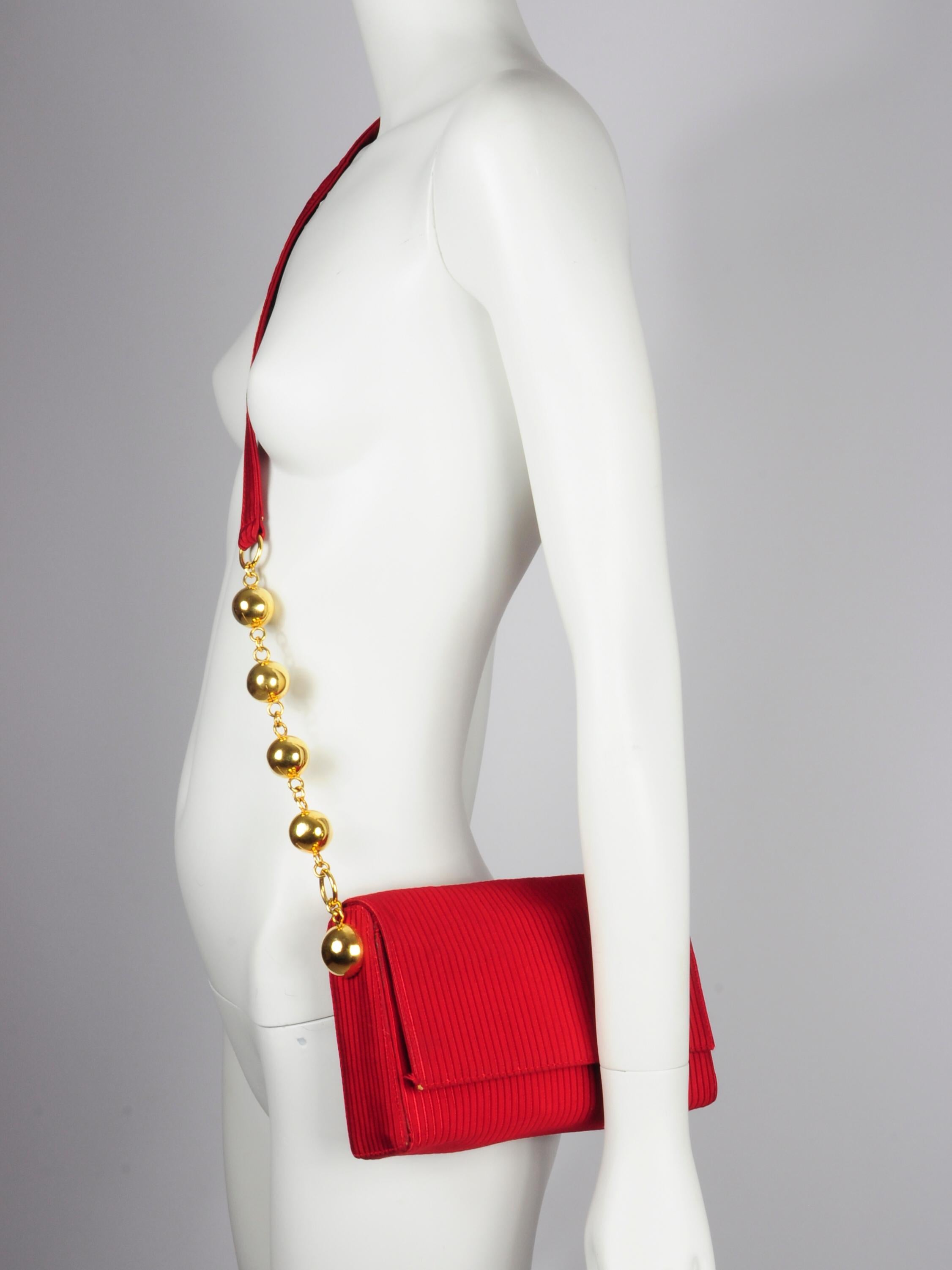 Gianni Versace Couture crossbody bag in red with gold spheres / balls on the strap from the 1980s. It has a beautiful round shaped top and flap that combines well with the golden spheres / balls on the crossbody strap. The fabric is striped