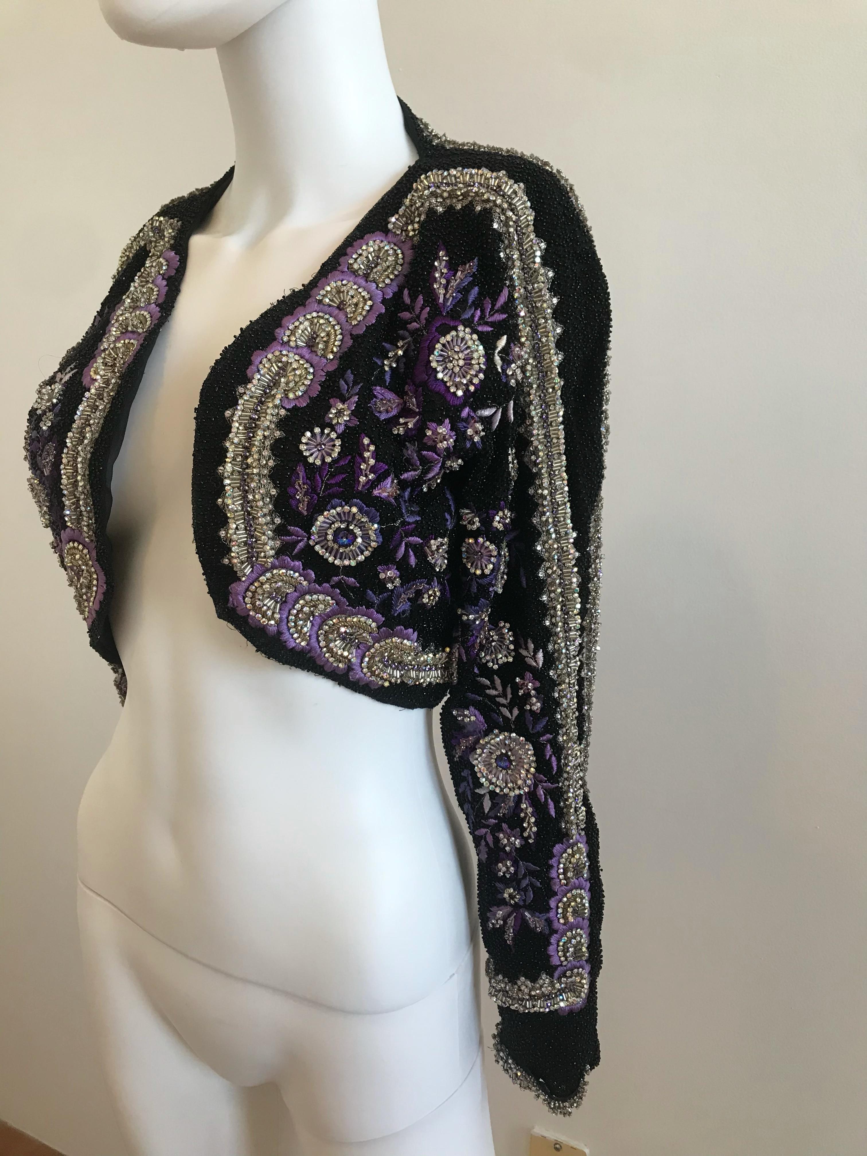 This Gianni Versace Couture Crystal Beaded and Embellished Cropped Bolero is extremely rare. It features a black beaded background with purple and rhinestone floral detailing. It is truly magnificent. The size tag has been removed. It fits a size US