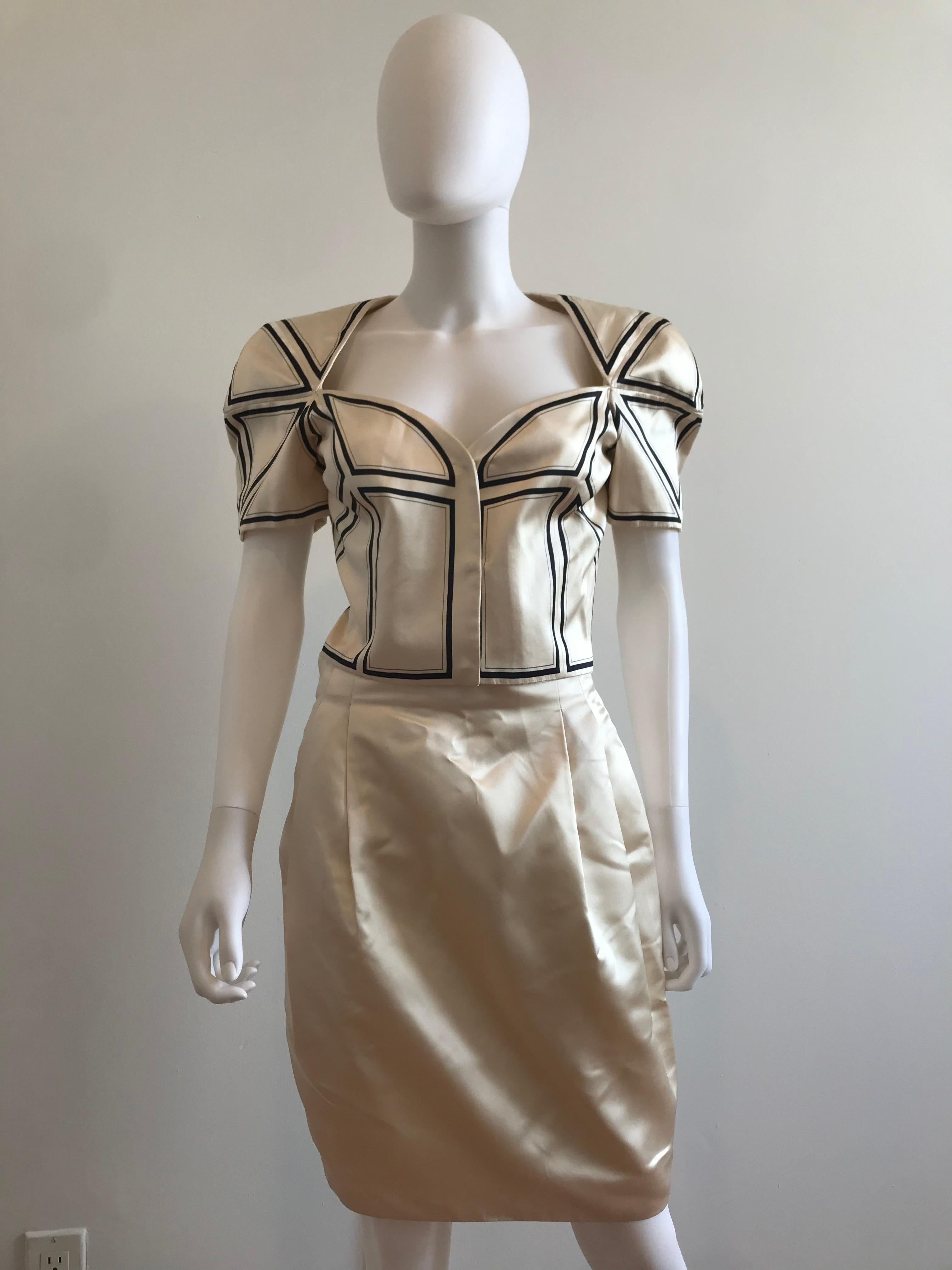 This Rare Gianni Versace Couture Origami Silk Cropped Blazer features pieced and stitched together white silk with black detailing. The sleeves are cap sleeved. The skirt accompanies the top in its elegant and sophisticated details. Suit Set. Size