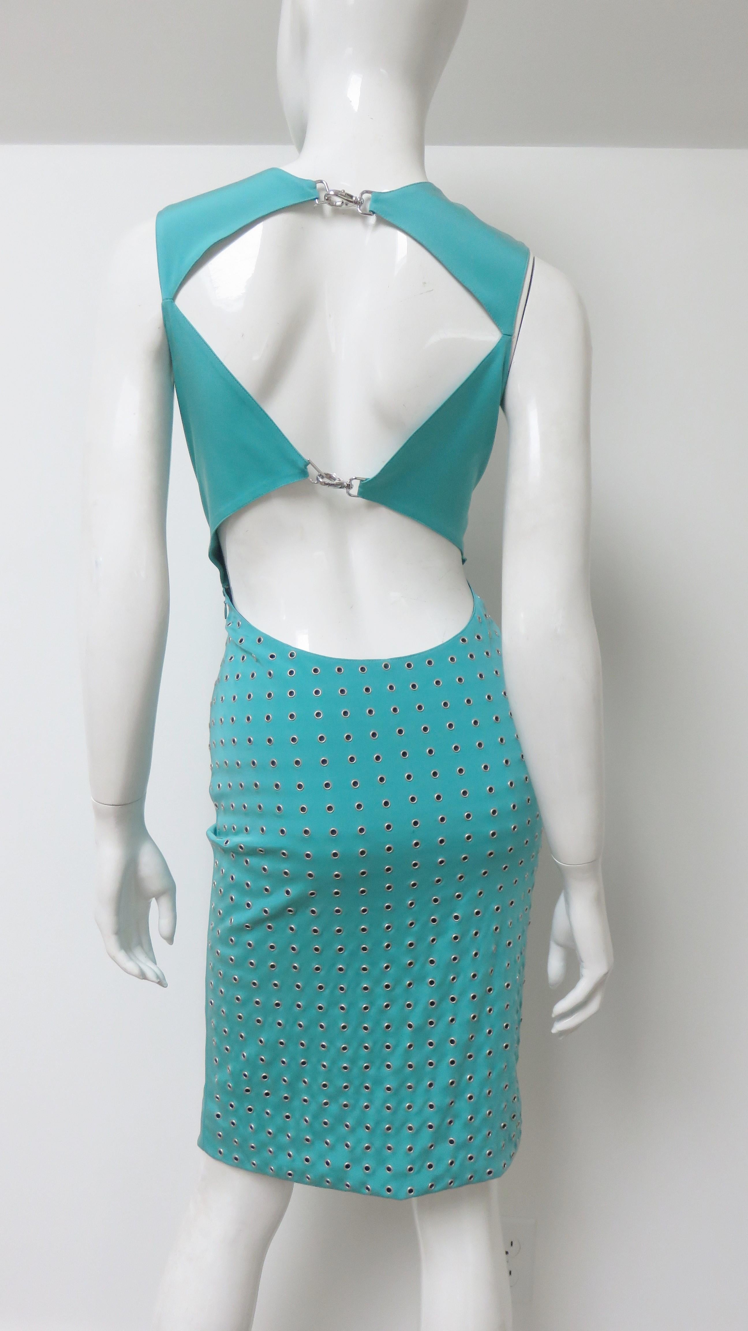 A fabulous turquoise stretch silk dress from Gianni Versace.  From the front is it a simple fitted sleeveless dress. The back is dramatic and detailed in contrast with cut outs at the upper back and waist closing with silver metal clasps. The skirt