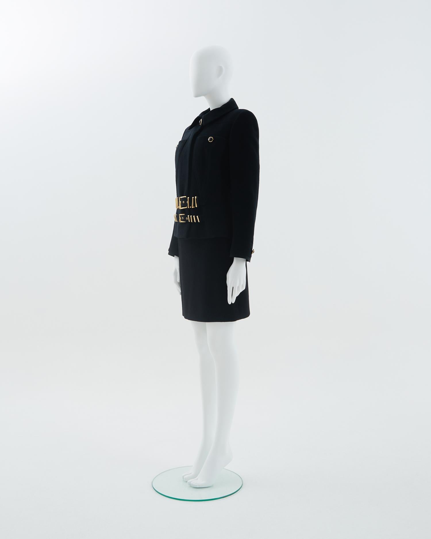 - ‘Miss S&M’ collection
- Sold by Skof.Archive
- Wool accented bondage buckle Gianni Versace cropped jacket and skirt set
- Designed by Gianni Versace
- Two topstitched belts with gold-tone metal loops in front and one on the back 
- Two pockets in