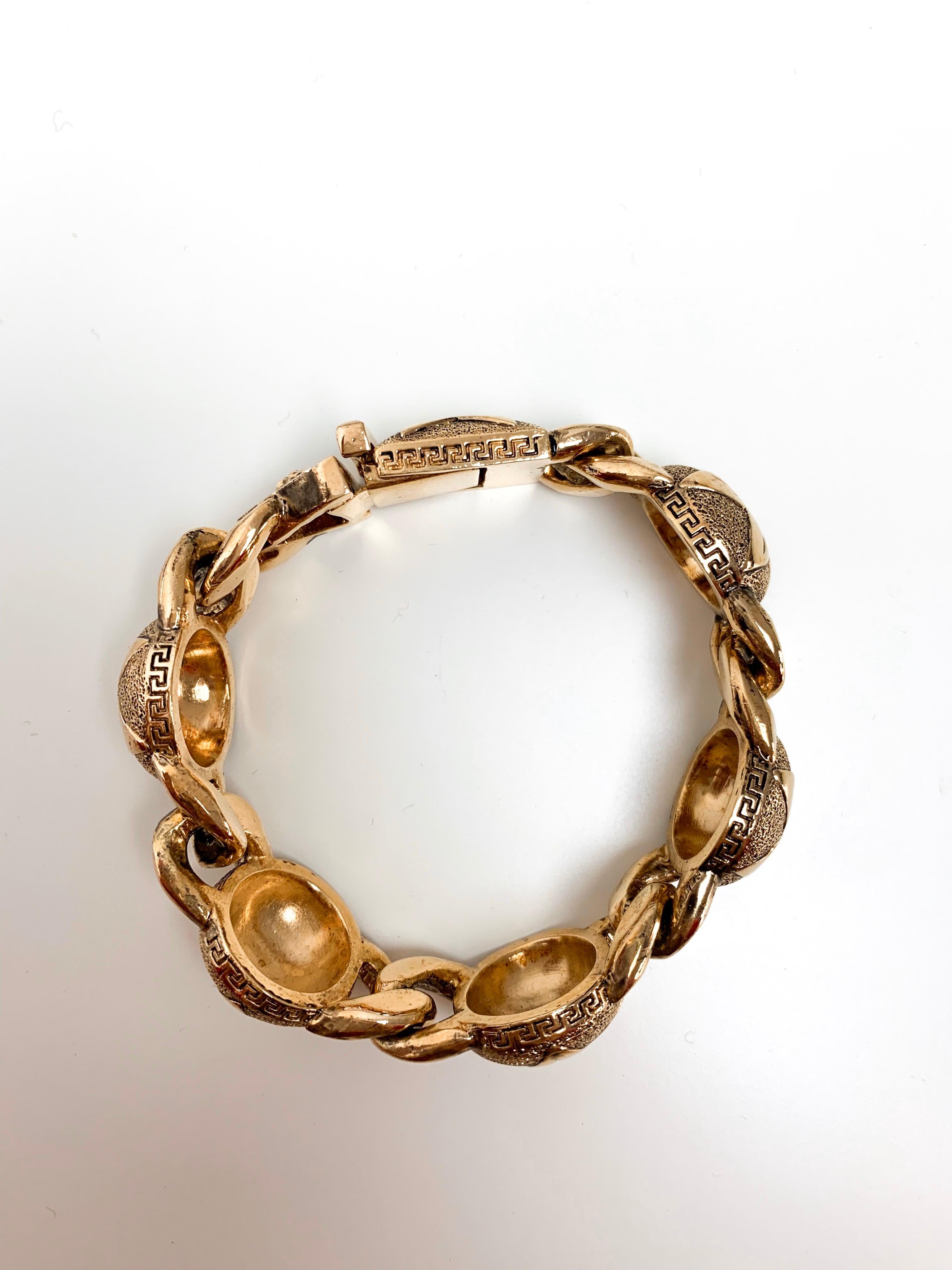 Fabriqué en Italie, ce bracelet en or de Gianni Versace présente cinq motifs circulaires avec l'emblème de l'étoile gravée, reliés par la traditionnelle boucle. Fini avec le symbole de la tuile grecque, ce bracelet reflète l'ère des années 90 que