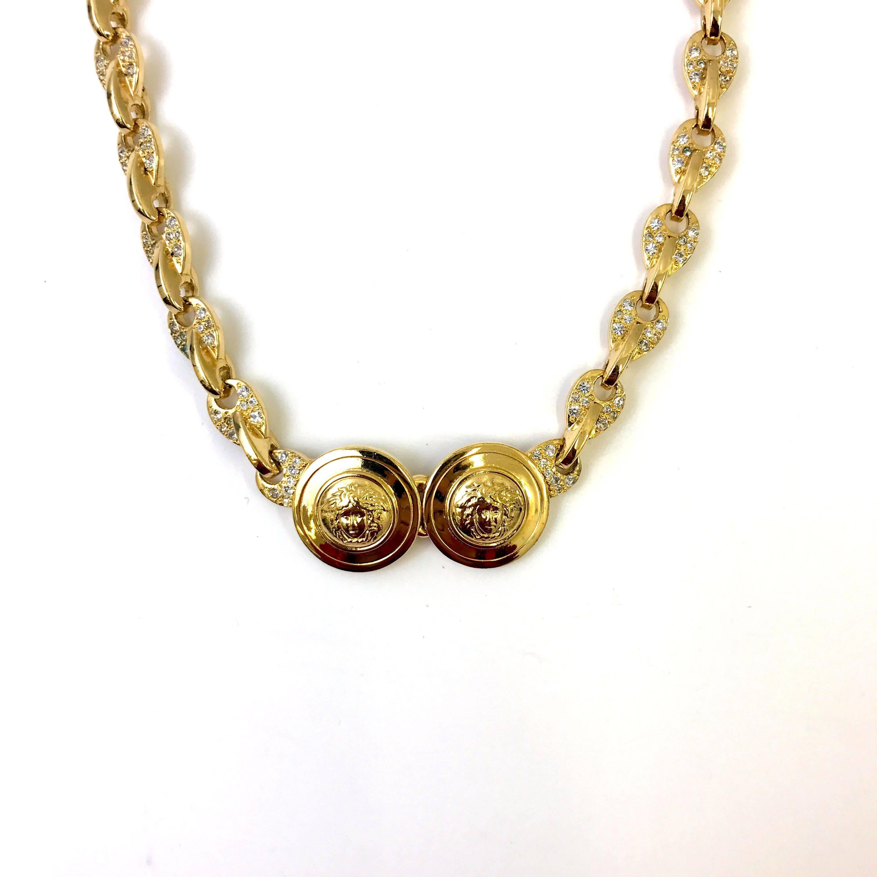 This is a iconic necklace from the famous Italian designer Gianni Versace from the 1990s. The necklace features a gold toned metal chain with a unique style link covered in rhinestones. In the centre of the chain there are two circle medallions with