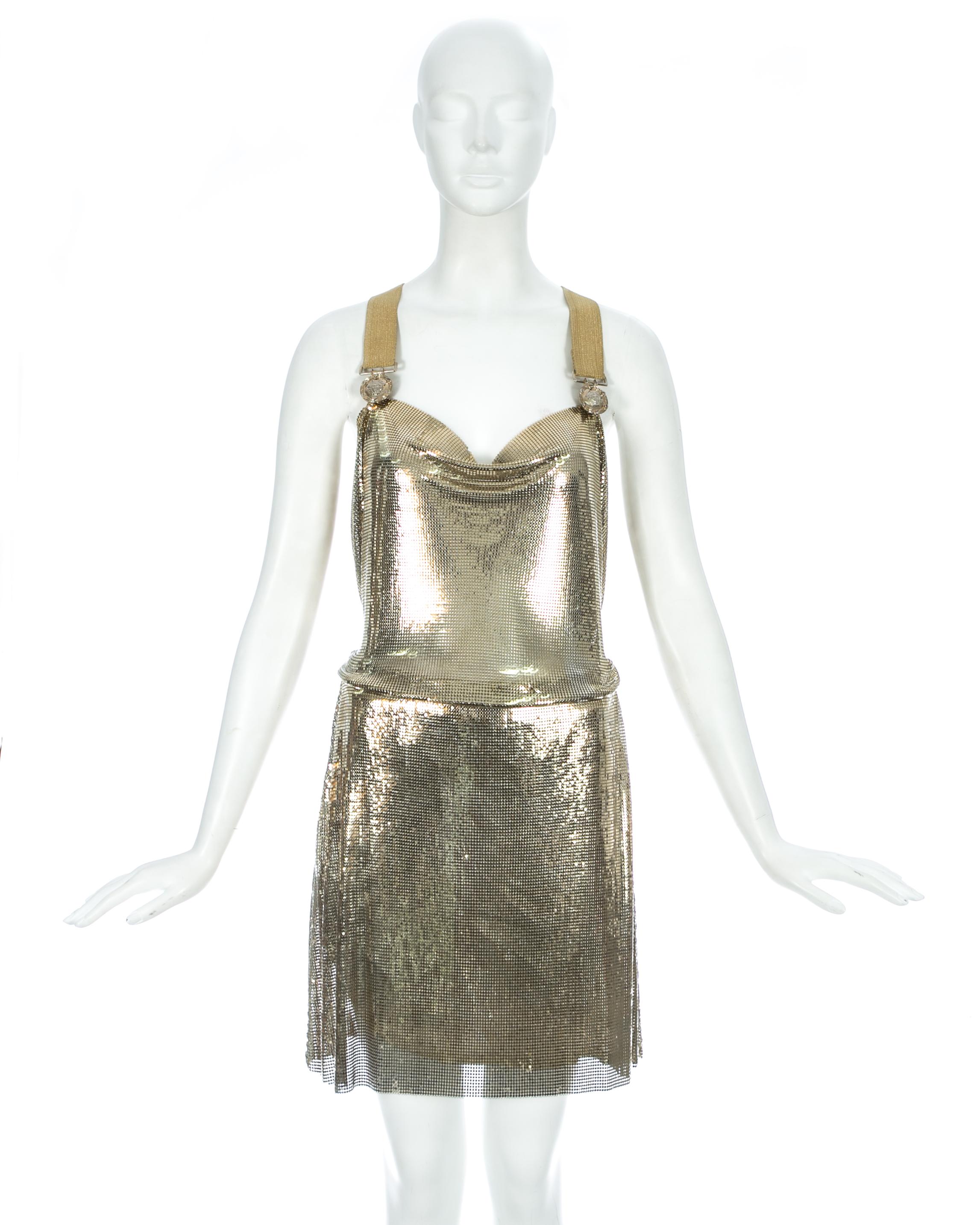 Gianni Versace; gold metal mesh evening dress comprises mini skirt with silk lining and a matching bodysuit with 2 gold plate medusa circular clasps, designed to be worn tucked into the skirt and drape over the waist band.

Fall-Winter 1994
