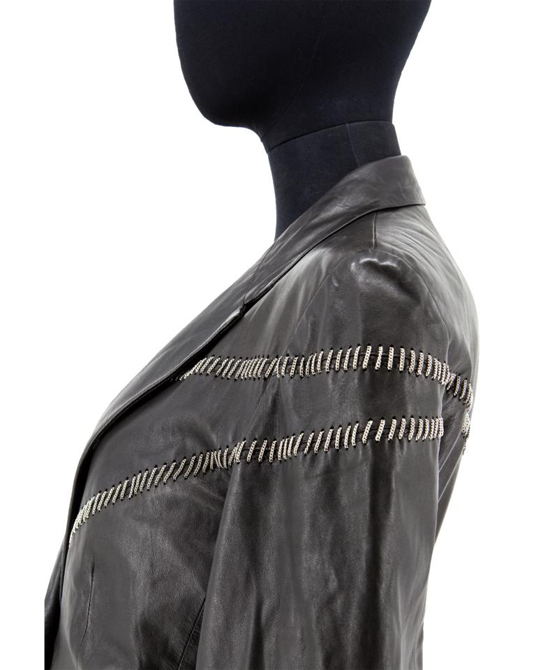 A late 1980’s Gianni Versace black matte plongé leather fitted panel jacket with large collar and revers, two-piece set-in sleeves with opening, two jetted pockets, featuring asymmetric style lines with a hand top-stitch of miniature chains