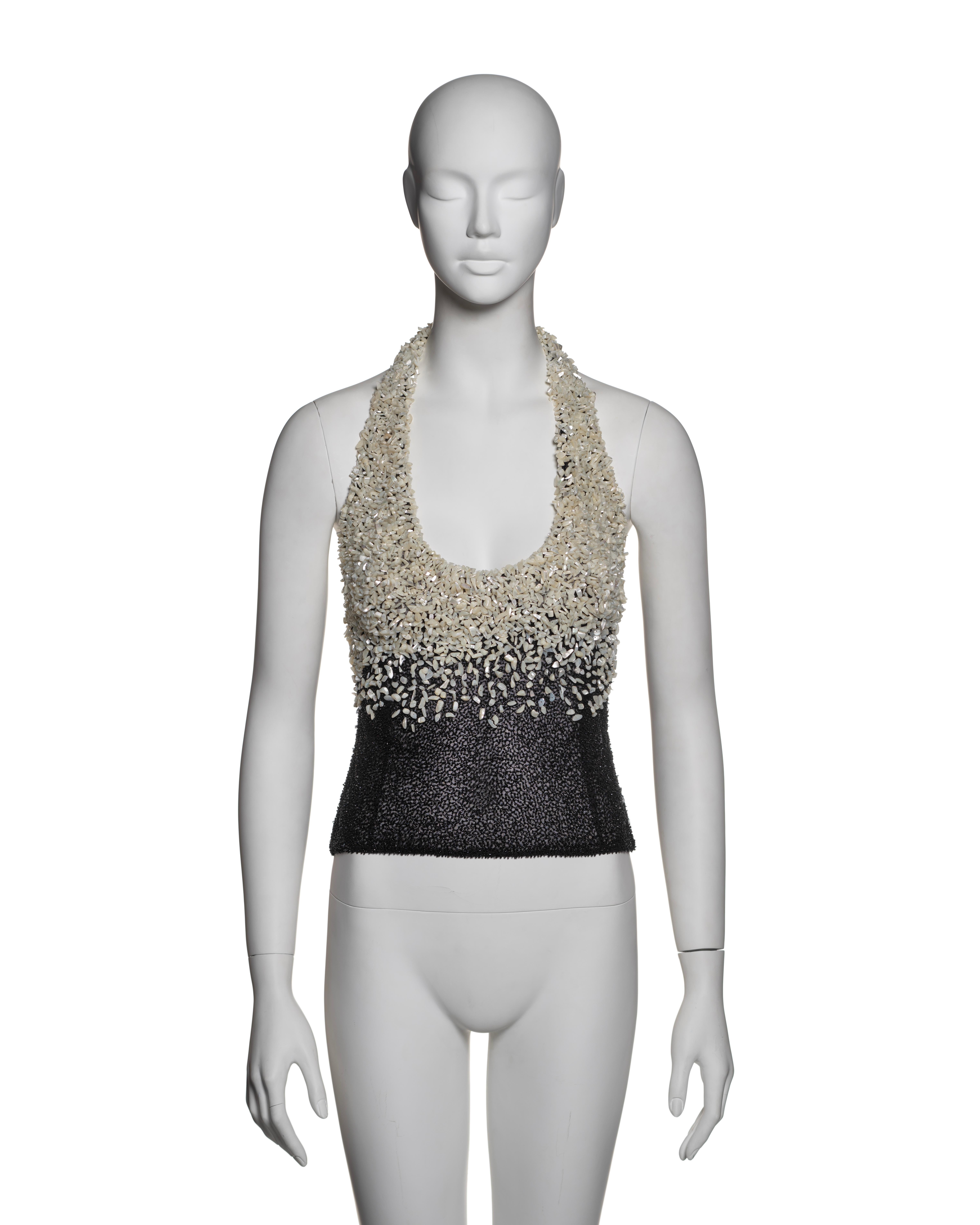 Gianni Versace, Fall-Winter 1999: A halter-style evening top featuring intricate embellishment with small, irregularly shaped mother-of-pearl beads densely applied to a black mesh base. The gradient design transitions from a heavy, ivory-toned