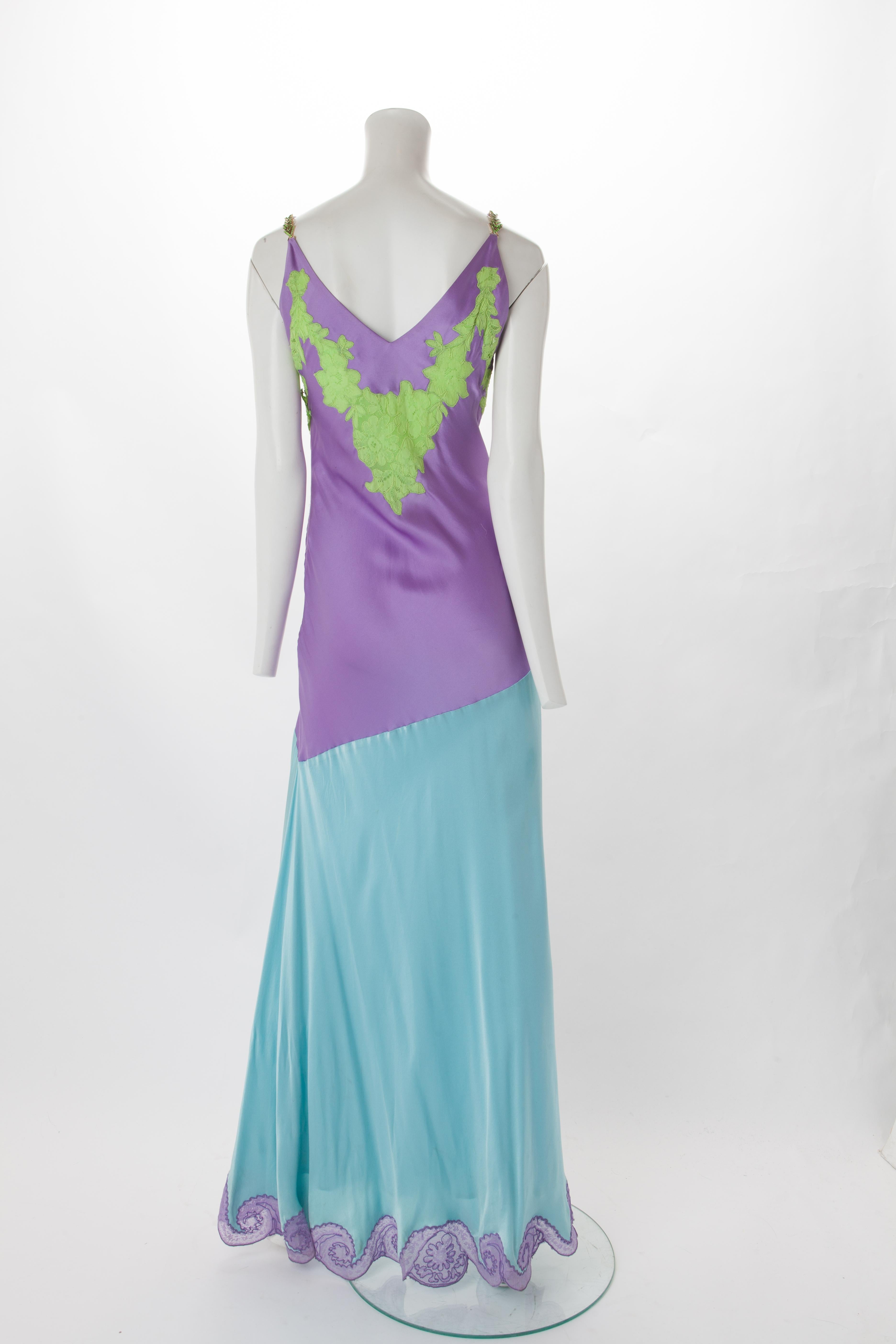 Gianni Versace Purple and Blue Satin Gown with Lace Appliqué, 1996.
Purple satin bodice with green lace appliqué at bust and blue satin skirt with purple lace appliqué along slit and hem.
Gathering at hip with gold with gold and emerald crystal bee