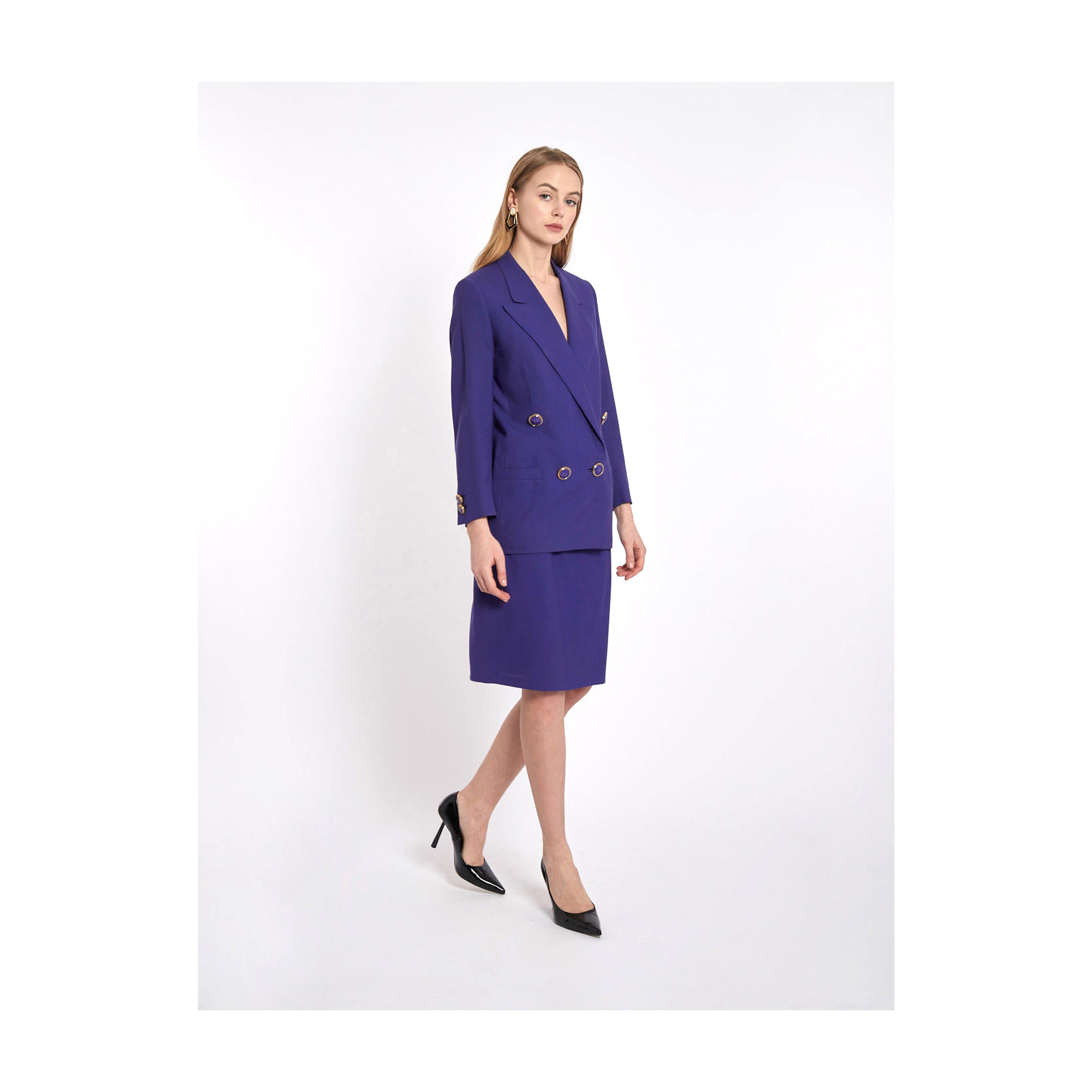This Gianni Versace jacket and skirt suit, labelled on the front, in bright purple is pure Eighties extravagance. The double-breasted jacket has a plunging neckline and it is decorated with large golden and purple buttons on the pockets and on the