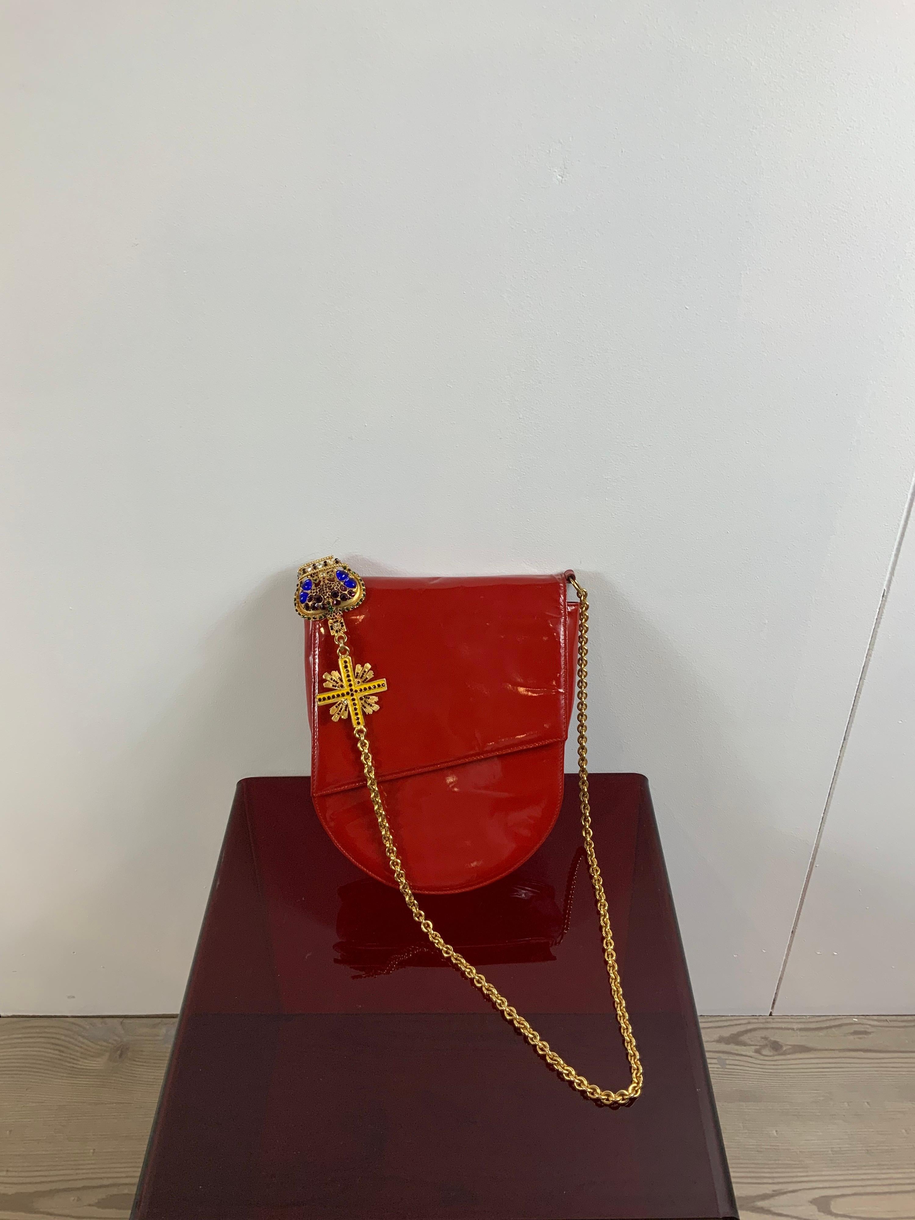 Gianni Versace vintage bag.
Red patent leather and gold hardware.
Featuring a shoulder chain and a cross & a crown as decorations. 
As you can see from the photos, the crown is broke and a little corner is missing.
Measurements 
height 26 cm
width