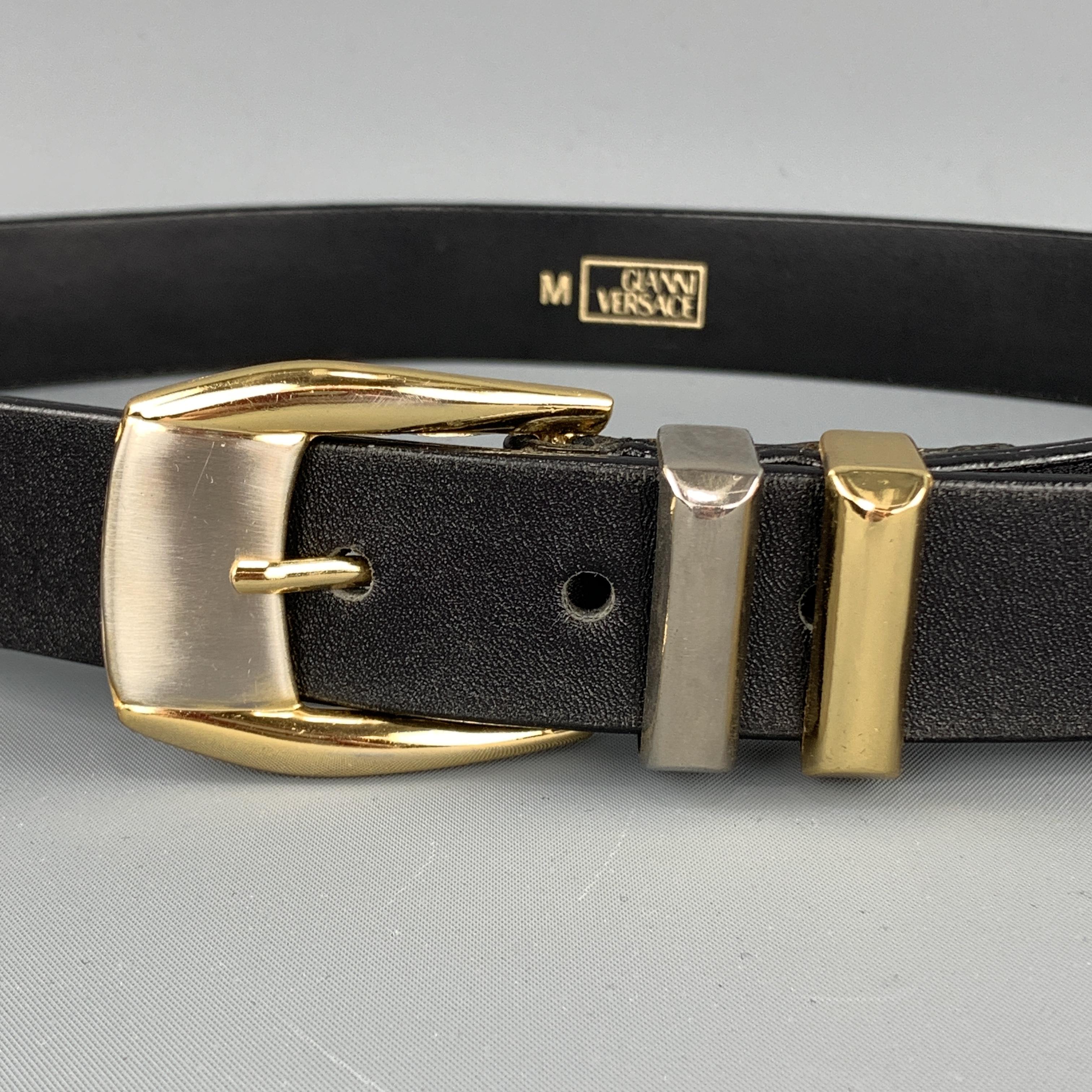 Vintage late 1980's - early 1990's GIANNI VERSACE waist belt features a smooth black leather strap with with silver tone embossed studs, gold and silver tone buckle with metal loops, and cutout hardware with Medusa head medallions. Removed from a