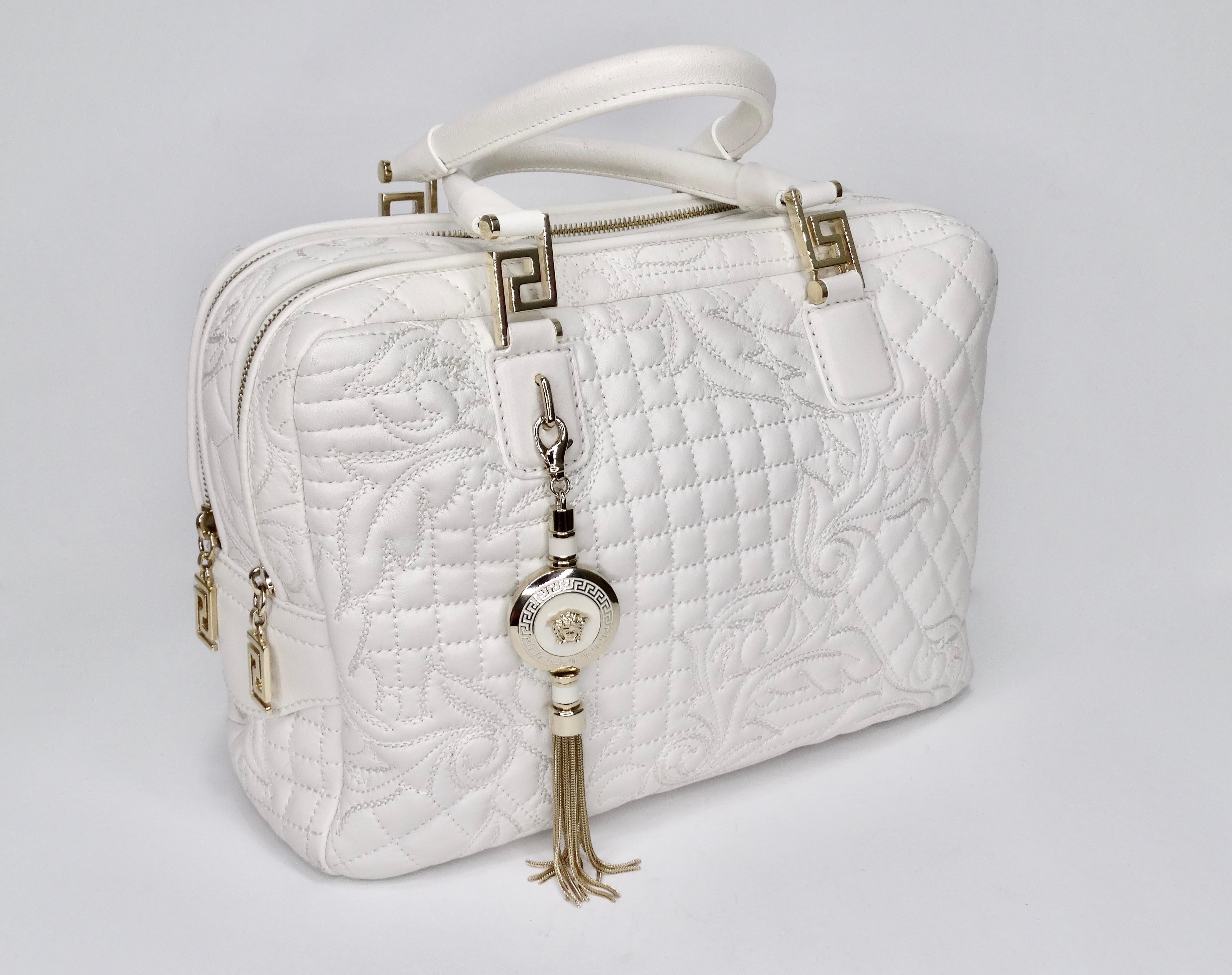 Calling all Versace lovers! Circa mid 2000s, this handbag is crafted from white leather and features quilted stitching with the signature Versace Baroque pattern, dual rolled handles, optional shoulder strap, gold toned Greek Key hardware and two