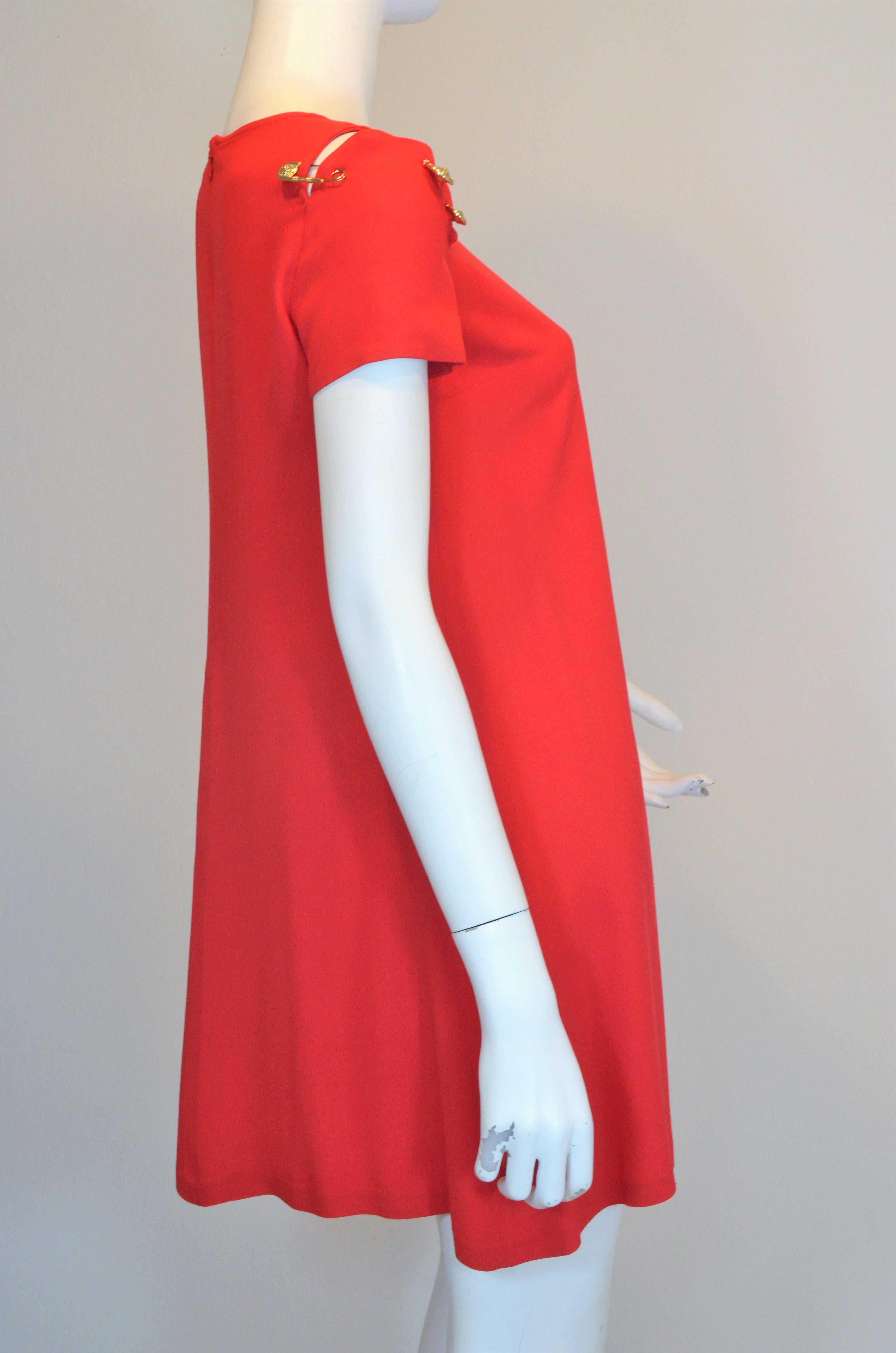 Gianni Versace VERSUS Red crepe dress features an a-line design with gold, signature Medusa safety pins attached at the shoulder that can also be removed and used as a brooch. Dress has a back zipper fastening, labeled size 40, made in Bulgaria,