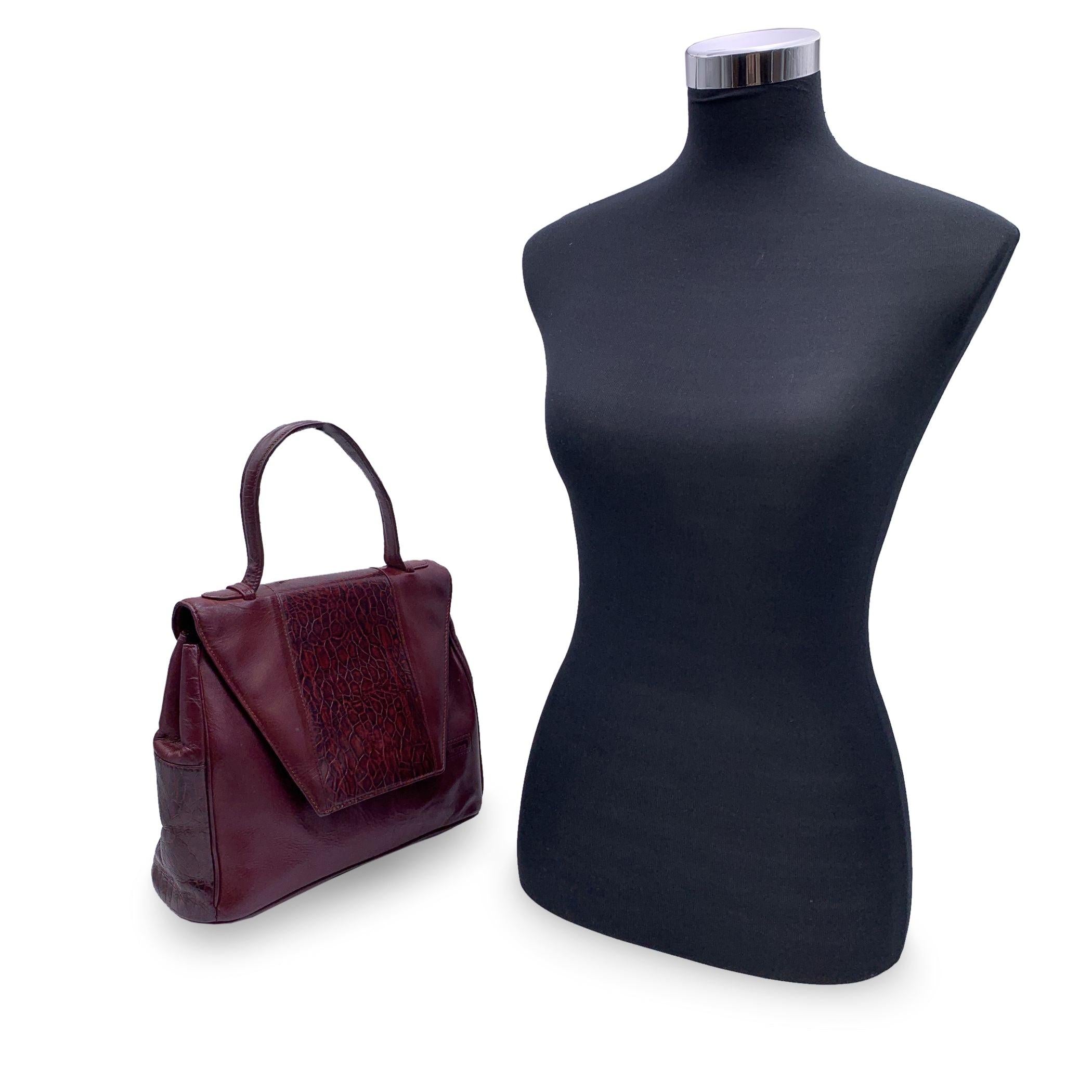 Magnifique sac à main vintage de Gianni Versace. Confectionné en cuir bordeaux, il présente un motif animalier gaufré sur le rabat avant et sur les côtés du sac. Poignées de transport sur le dessus. Rabat avec fermeture à bouton magnétique. Doublure
