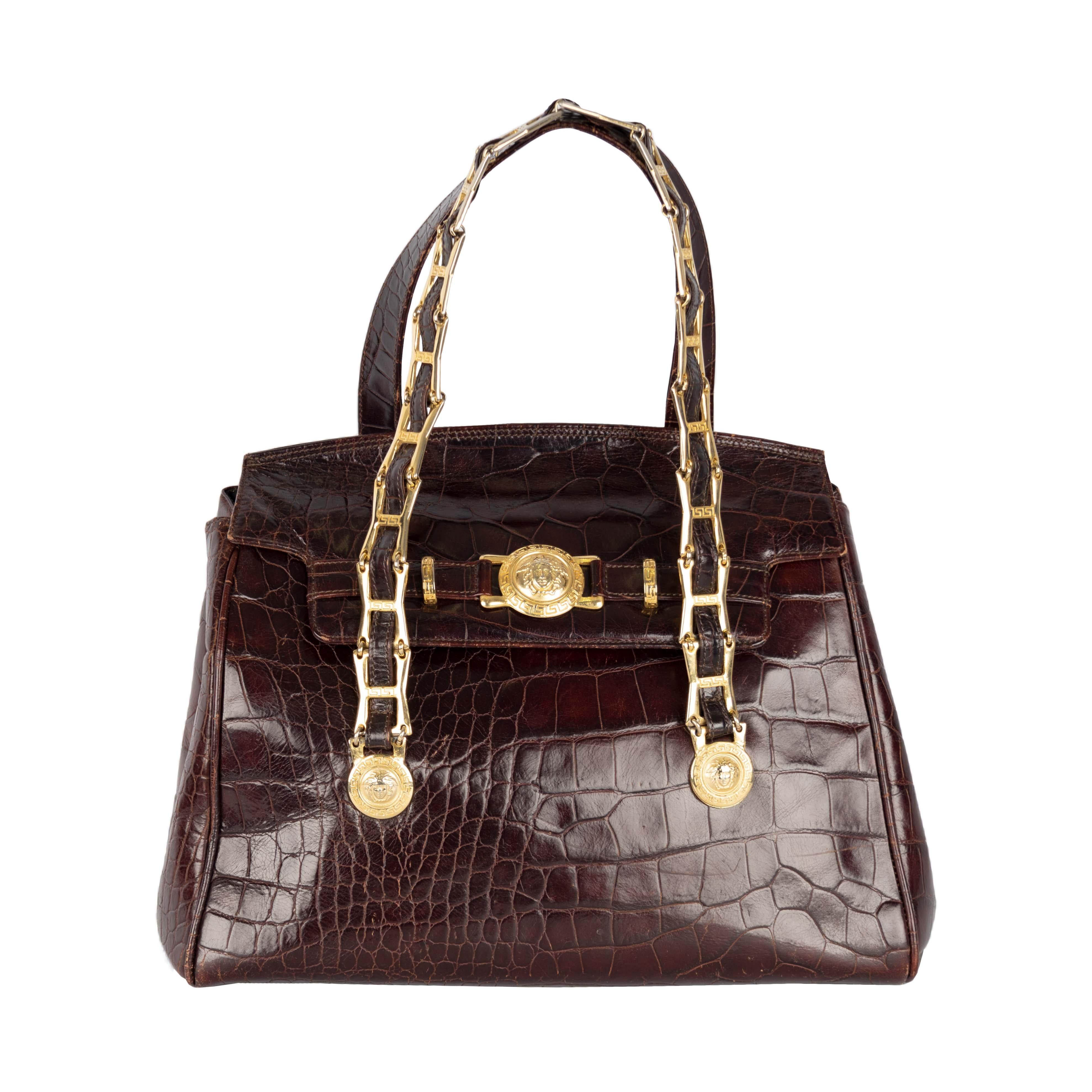 A rare vintage handbag by Gianni Versace in crocodile pattern embossed leather with a wallet and a passport/document holder. The bag features the brand's iconic golden medallion over the flap and at the end of the straps. The front handle strap is