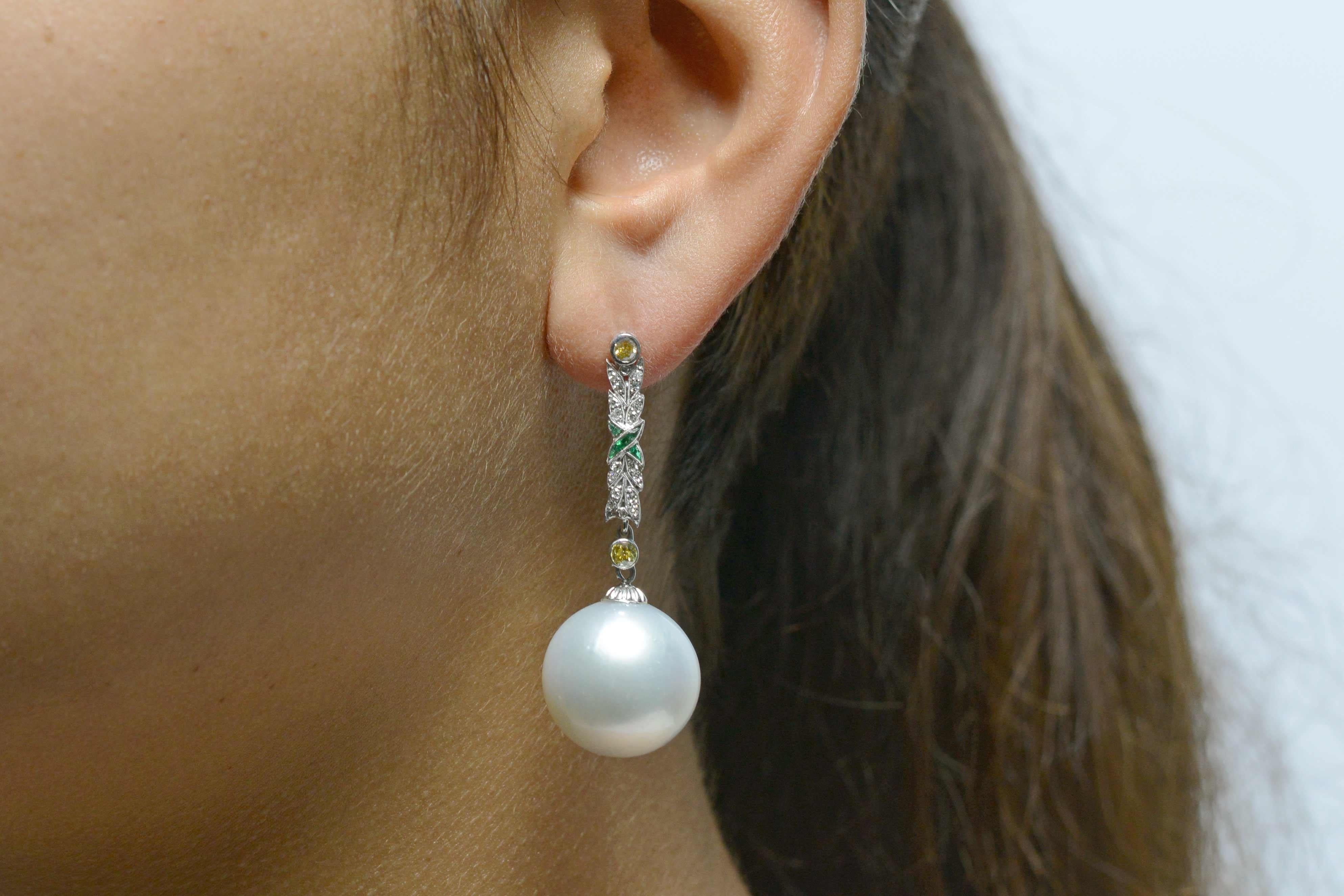 A most magnificent pair of giant South Sea Pearl drop earrings that dangle dramatically, suspended from dazzling yellow and white diamond sections bisected with an alluring emerald criss cross. Fabricated from platinum with great attention to