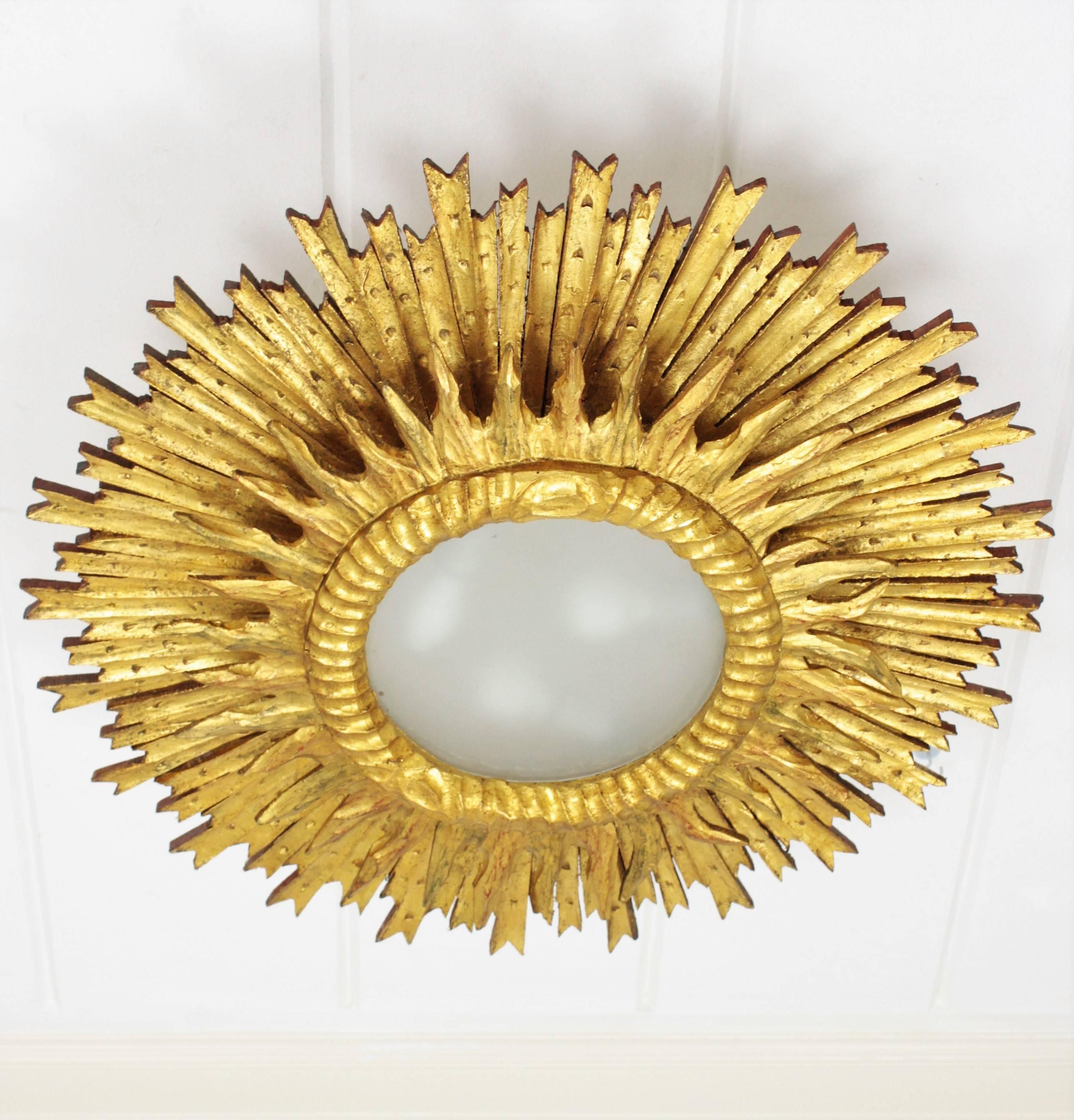 A huge double layered carved and giltwood sunburst light fixture with gold leaf finish. This absolutely stunning sunburst light fixture has a frame with large beams and a small frame with short beams surrounding the central frosted glass difusser.