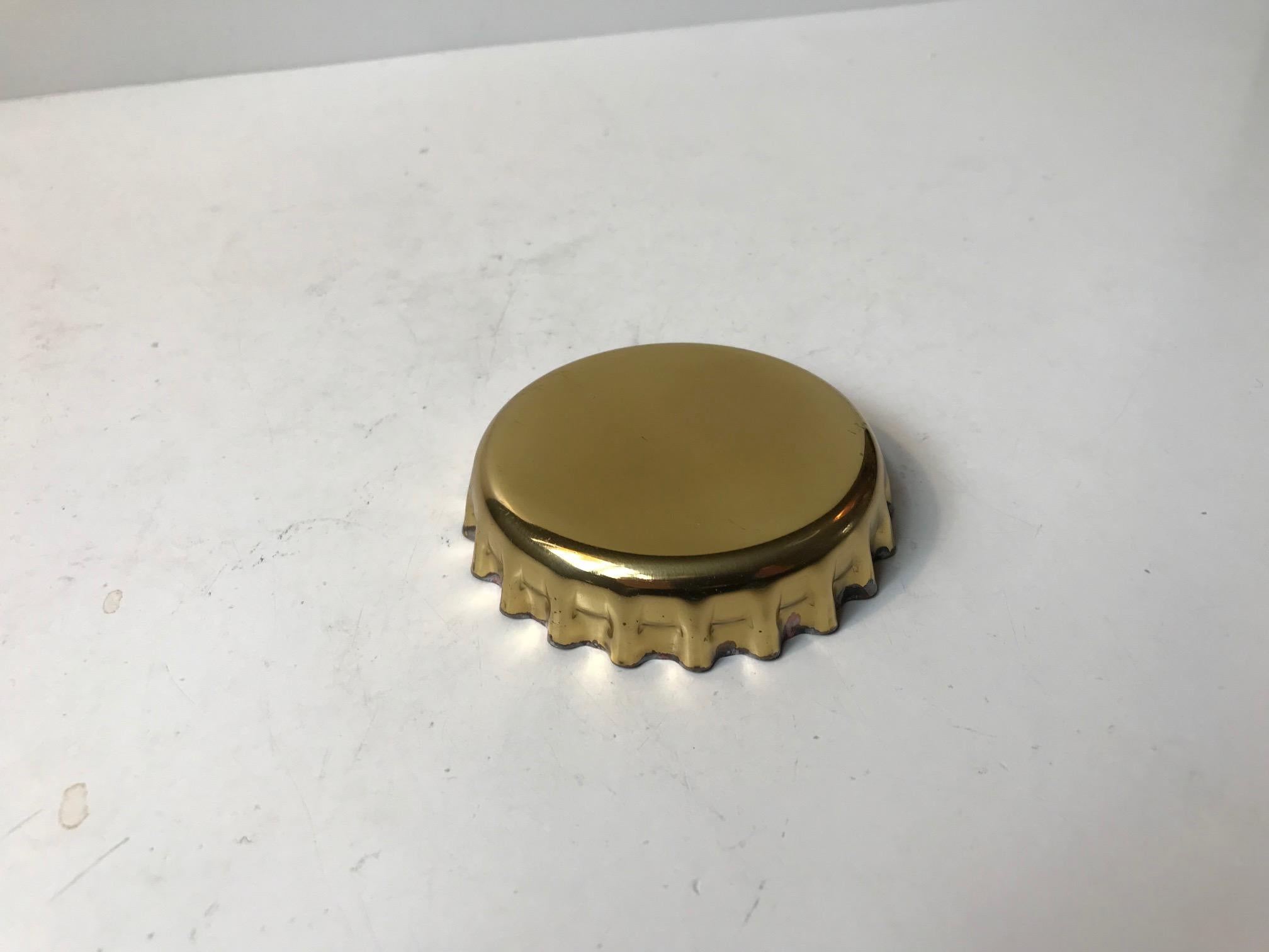 Manufactured in 1981 this curious bottle cap shaped opener is made from sculpted brass with a 'opener' mechanism in stainless steel. It is signed to the inside: Georg Jensen Design, Denmark, 1981.