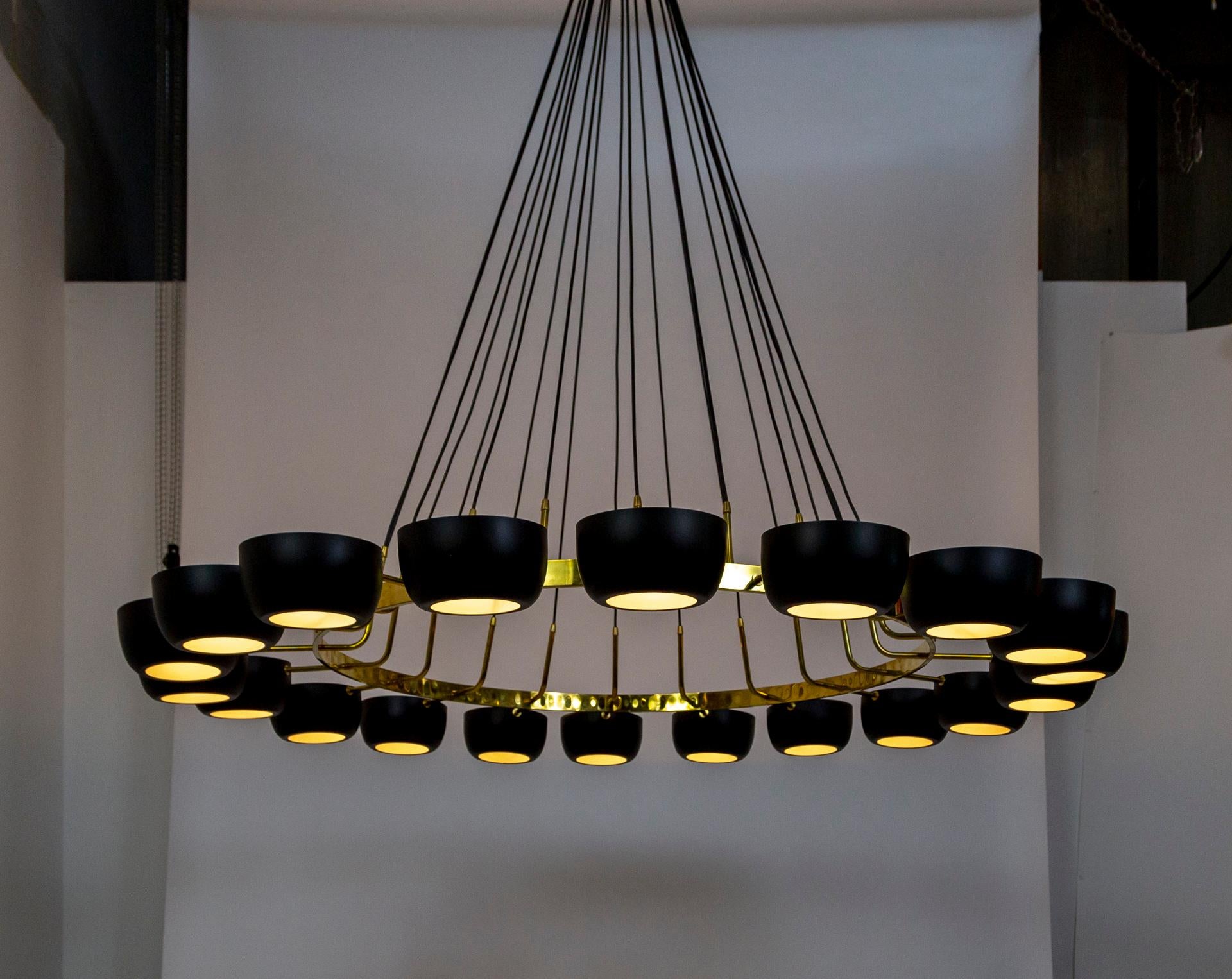 A huge, contemporary chandelier is made in Italian Mid-Century Modern style. It has a brass, ring structure that holds 20 lights with open-ended, bowl shades, projecting light both up and down. The shades are satin black, matching the black cords