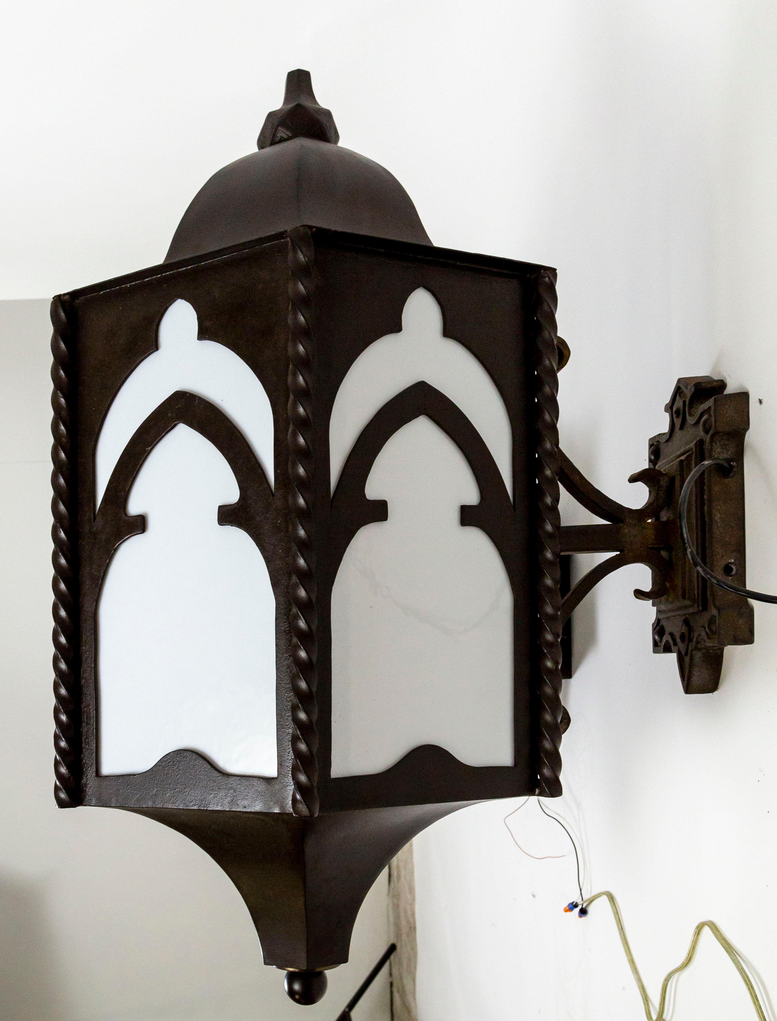 A pair of gigantic, iron wall lanterns in a dome-capped, hexagon shape, with gothic arched panels and twisted column accents. They have newly installed, white glass plates and one medium base socket. Measures: 25.25