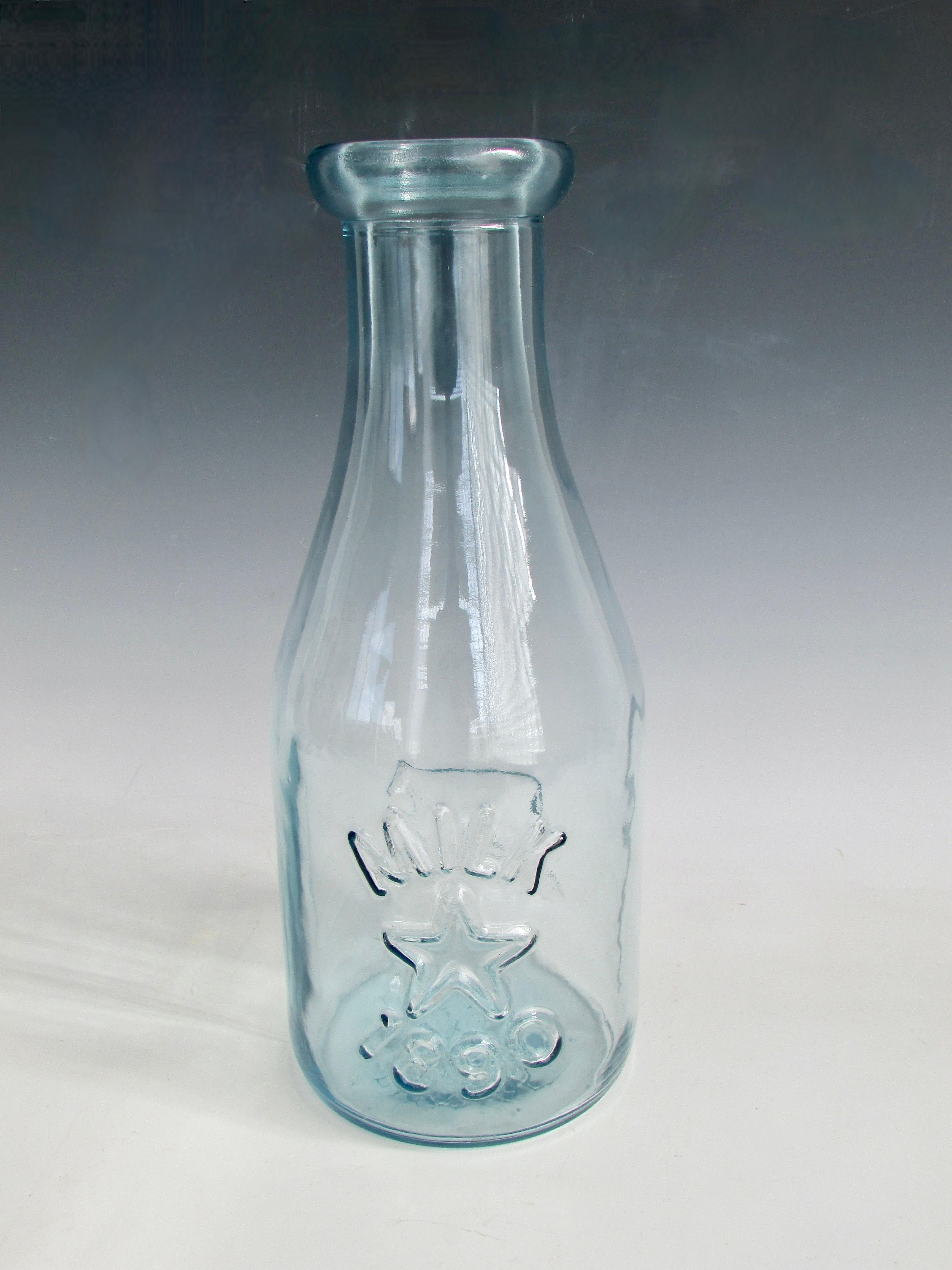 Riesige Milchflasche aus blau getöntem Glas. In eine Form geblasen. Kuhbild auf der einen Seite, Stern und 1890 auf der anderen Seite. Großer Stern auch auf der Unterseite. Wahrscheinlich in der zweiten Hälfte des 20. Jahrhunderts. Großes Geschäft
