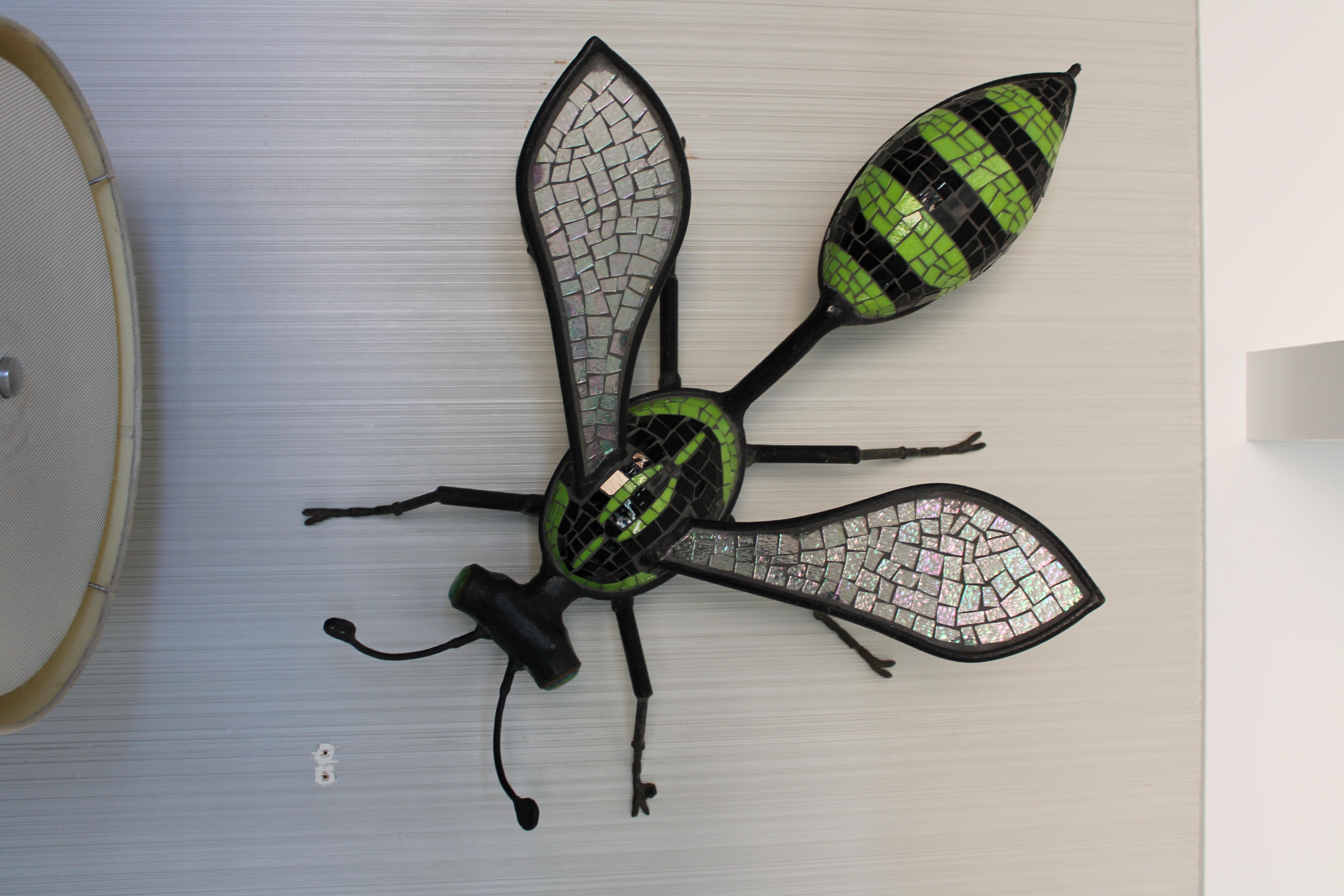 A vintage wrought iron wasp sculpture with colorful glass mosaic inlay. Tiffany style iridescent glass eyes. Wings layered with clear and iridescent glass tiles. Wall sculpture measures an impressive 31