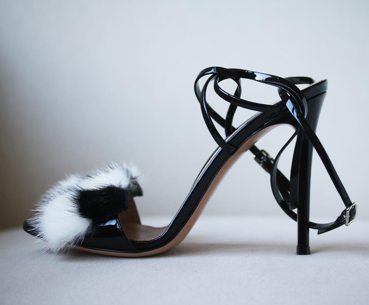 Black, patent-leather. Open toe, patent-leather covered high stiletto heel. Black and white block-colour front mink-fur strap. Skinny crossover side and heel straps. Black patent-leather buckle fastening. Nude leather insole and sole. Made in Italy.