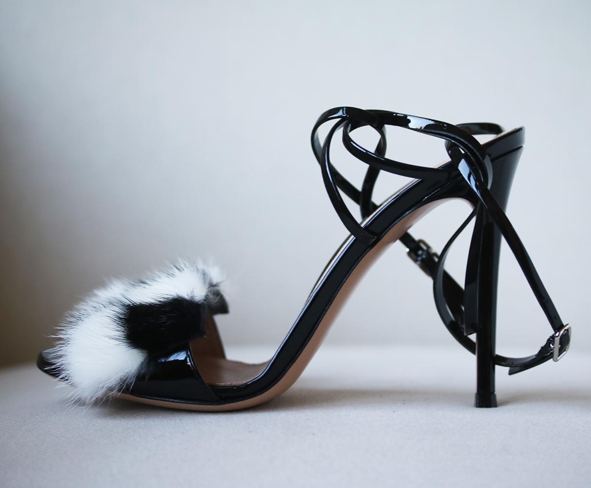 Black, patent-leather. Open toe, patent-leather covered high stiletto heel. Black and white block-colour front mink-fur strap. Skinny crossover side and heel straps. Black patent-leather buckle fastening. Nude leather insole and sole.  Made in