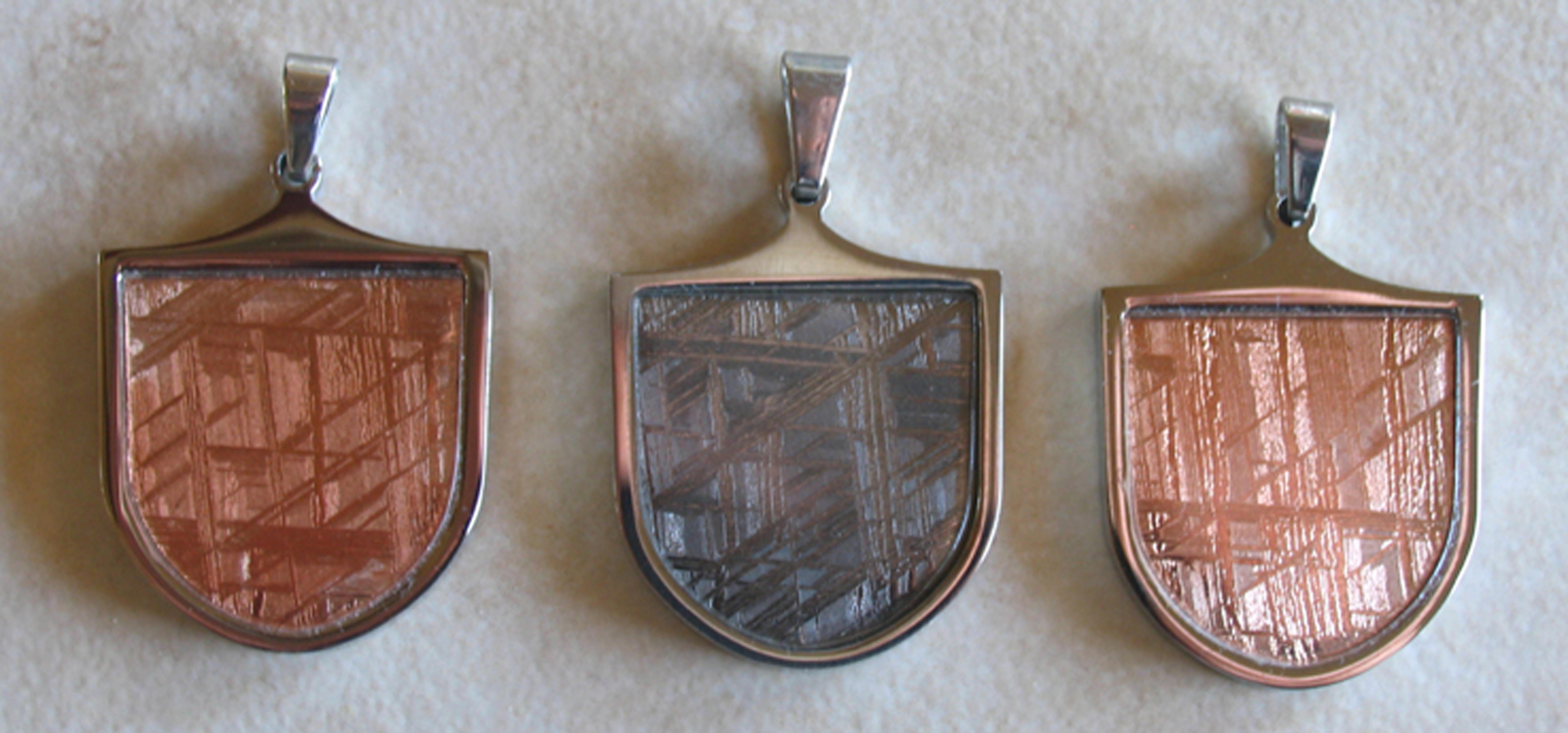 Stainless Steel Pendants containing slices of the Gibeon Meterorite (Africa). The two reddish pieces have been Rose Gold Plated 
and the silver colored one is Silver Plated. On the back is stamped Gibeon Meteorite.  Though we have been known for