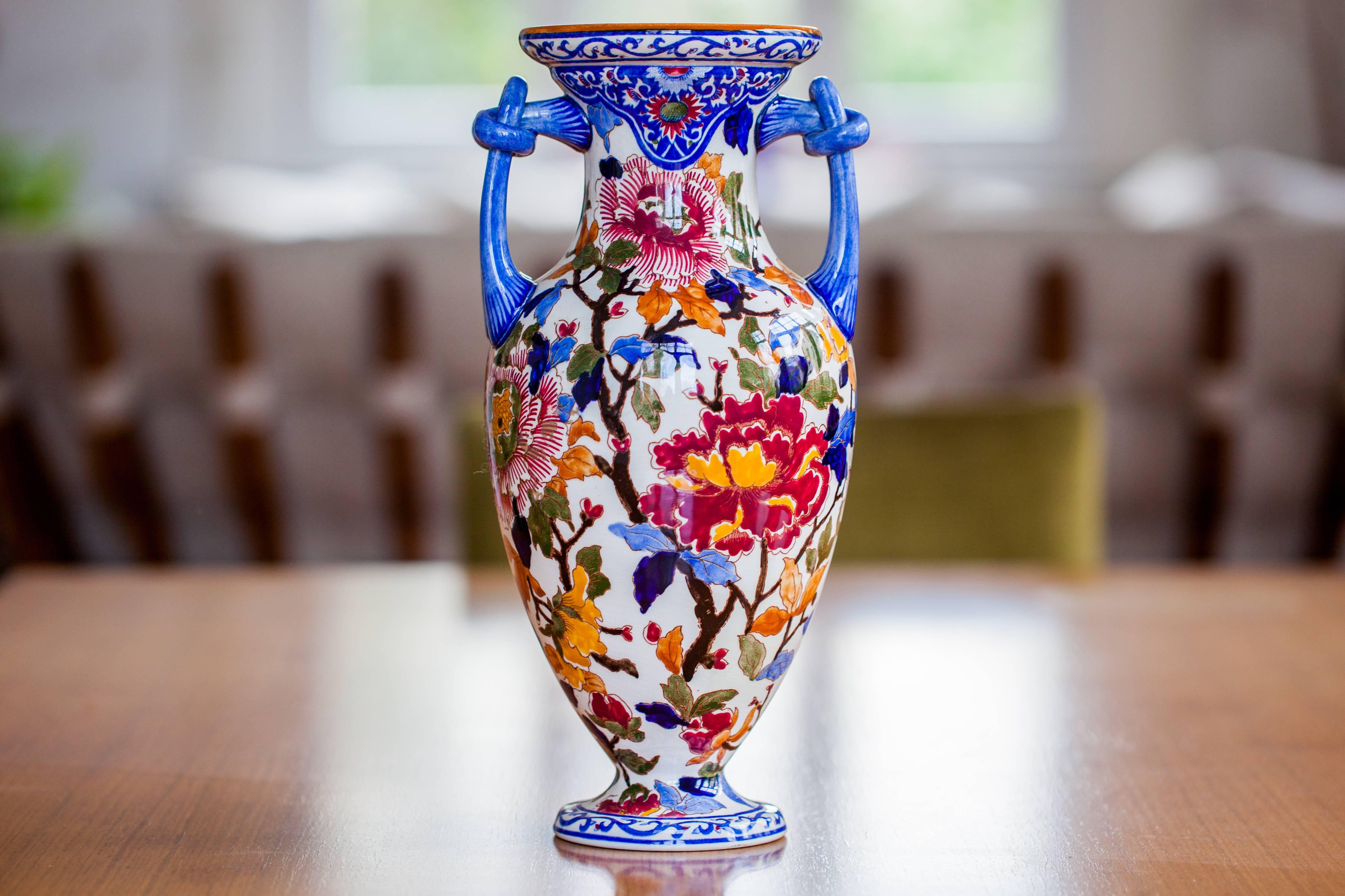 Large old Gien faience vase with multicolored floral decoration on a white background.
It is baluster shaped, amphora, two blue handles in the shape of a sliding knot, 