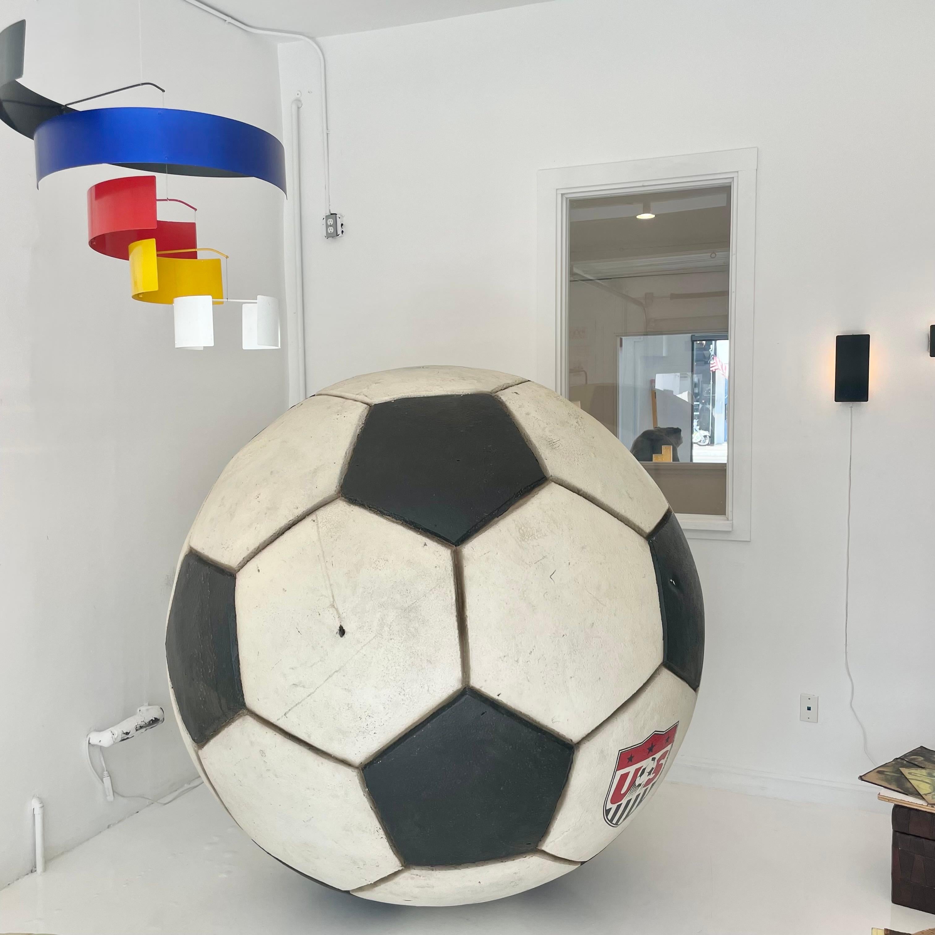 Gigantic soccer ball made of very hard foam. Weighted ball inside so that it stays where you place it. Metal loop on top for hanging from the ceiling if desired. US MENS SOCCER logo on the front. Approximately 80 pounds. Great coloring. Some scuffs,