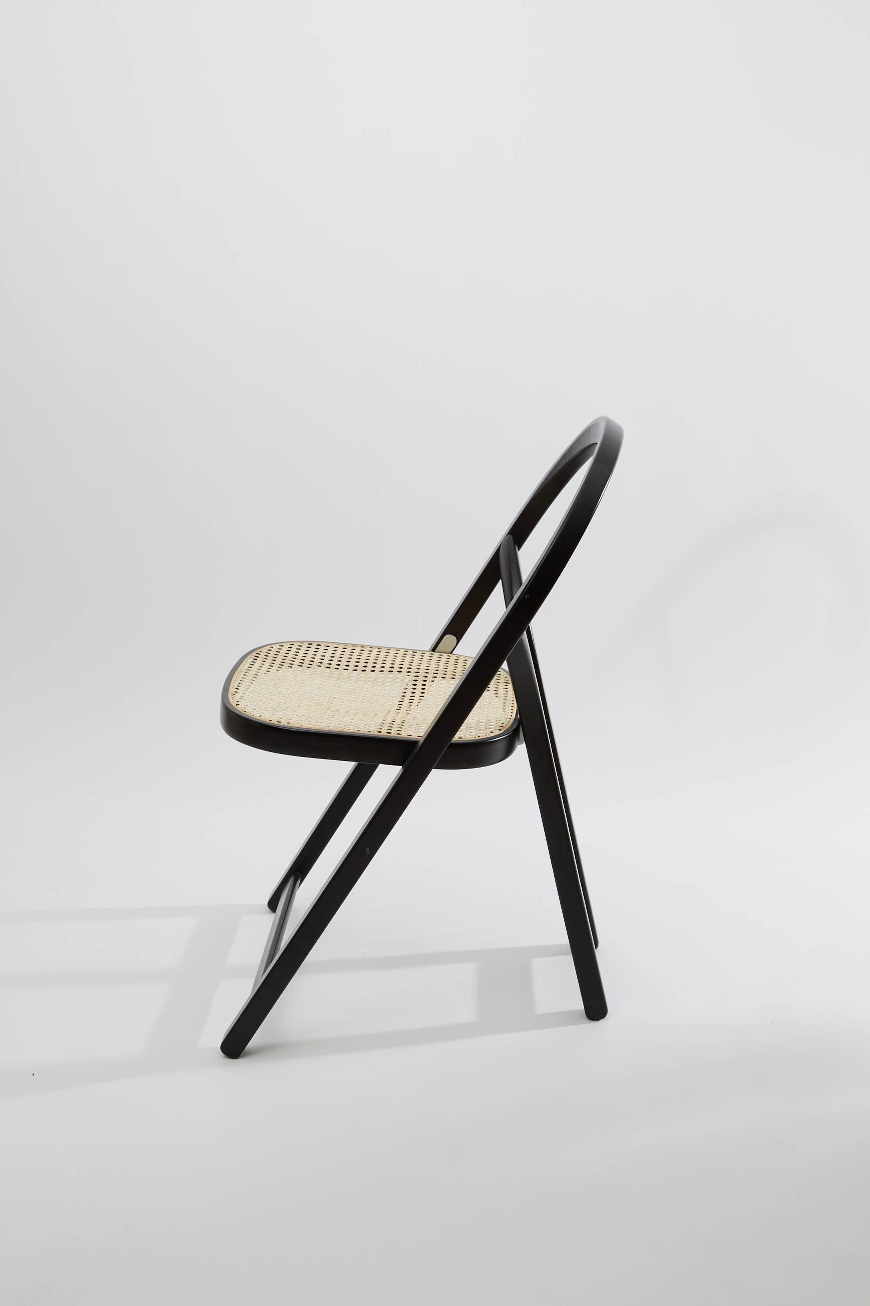 Arca chair design by Gigi Sabadin in 1974.
Crassevig edition.

Folding chair. 
Structure in black lacquered solid ash, steam bent. 
Seat in rattan.

Award: Selezione d’Onore del Compasso d’Oro 1979.